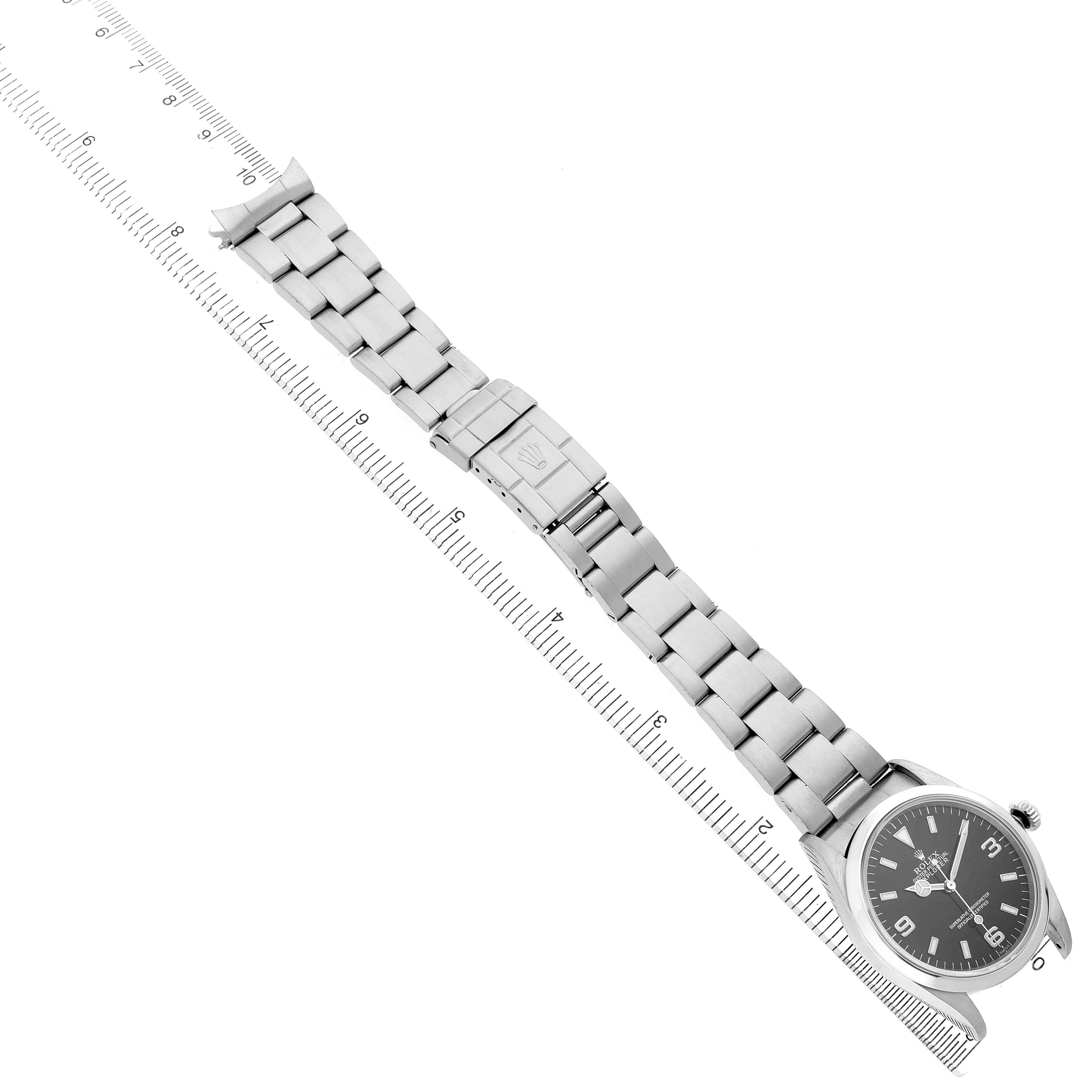 The Rolex Explorer 14270 Men's Stainless Steel Black Dial watch is shown from a top-down angle, displaying the full bracelet and clasp beside a ruler for scale.