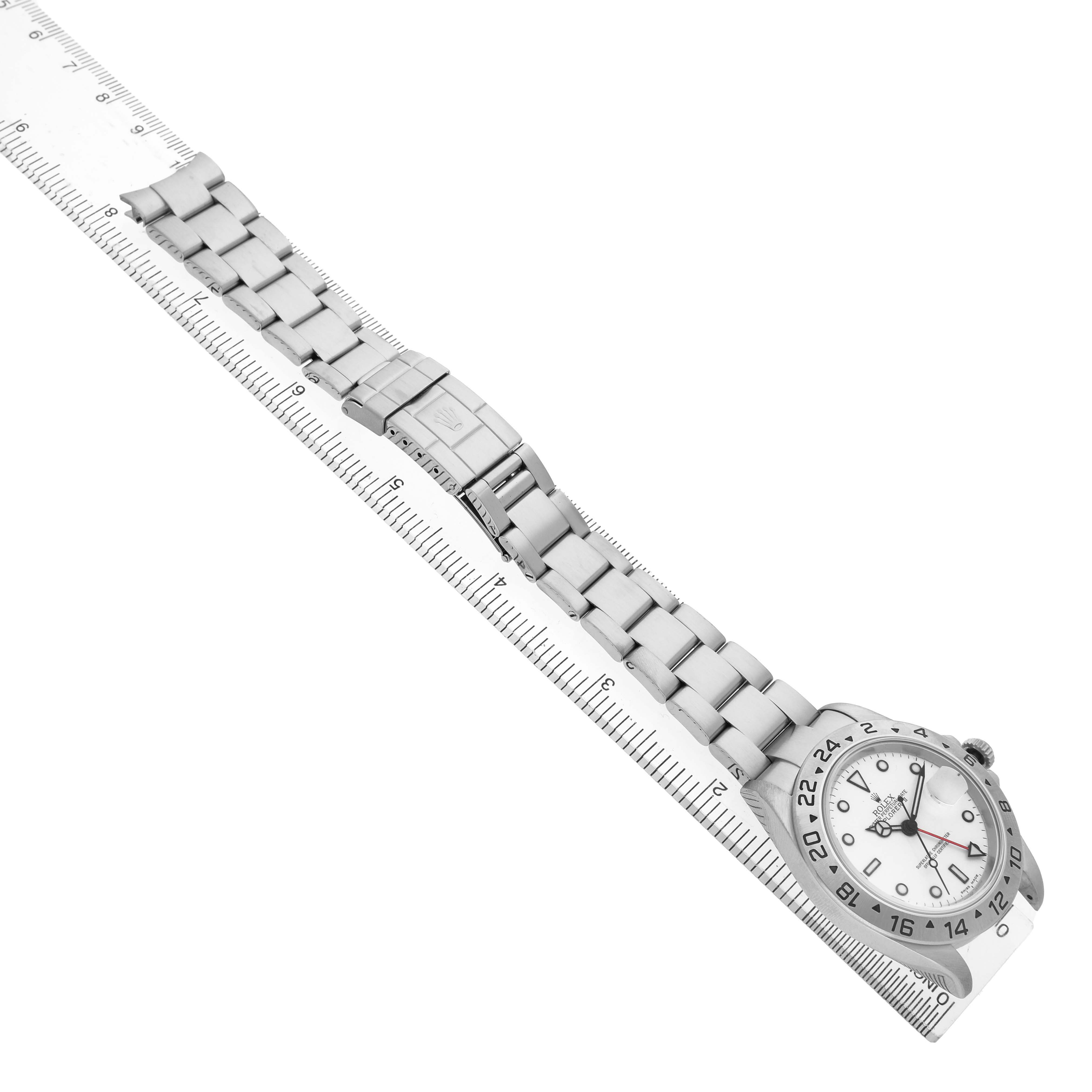 The Rolex Explorer 16570 Men's Stainless Steel White Dial watch is shown from a top view, featuring the face, bezel, and full bracelet laid alongside a ruler.