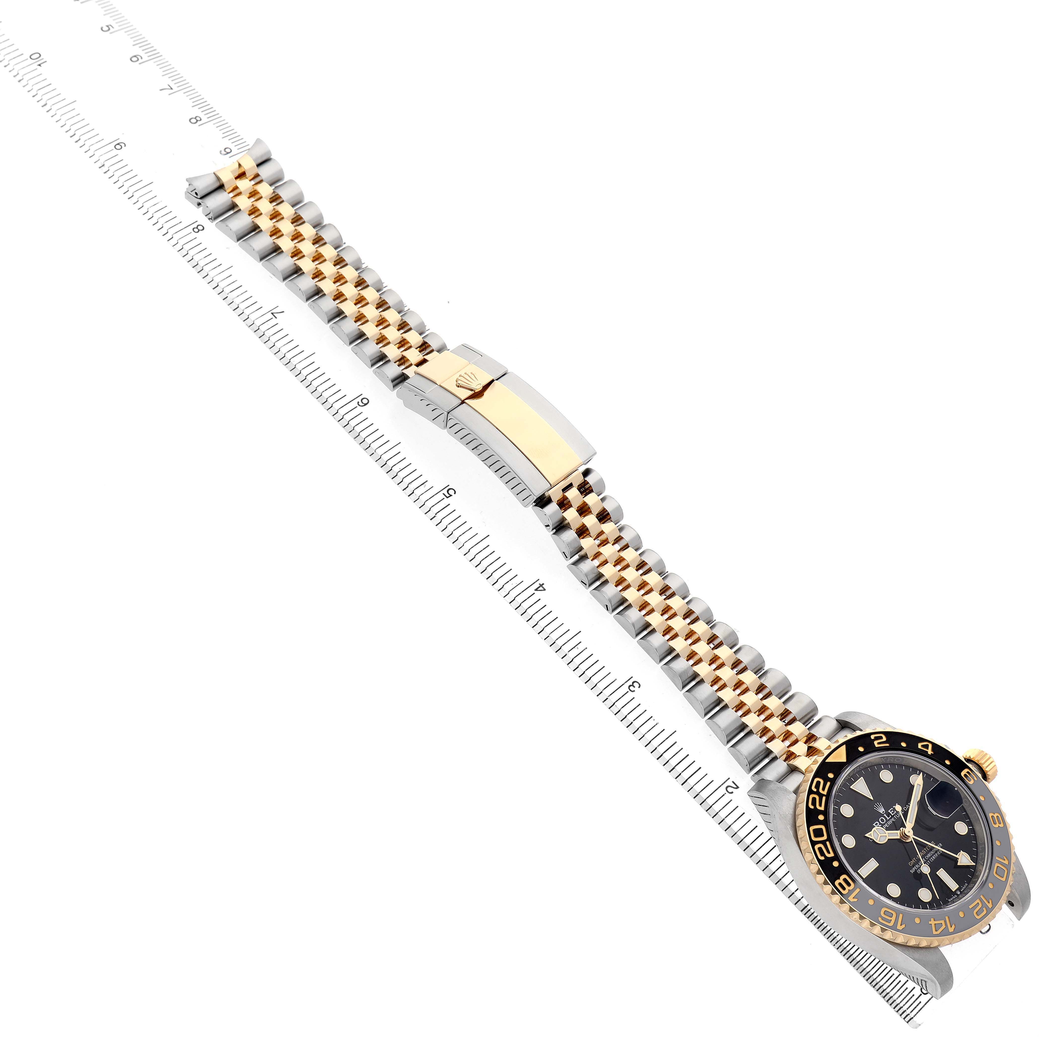The image shows a Rolex GMT-Master 126713 Men's Stainless Steel Black Dial watch at an angle highlighting the watch face, bezel, bracelet, and clasp with a ruler beside it.