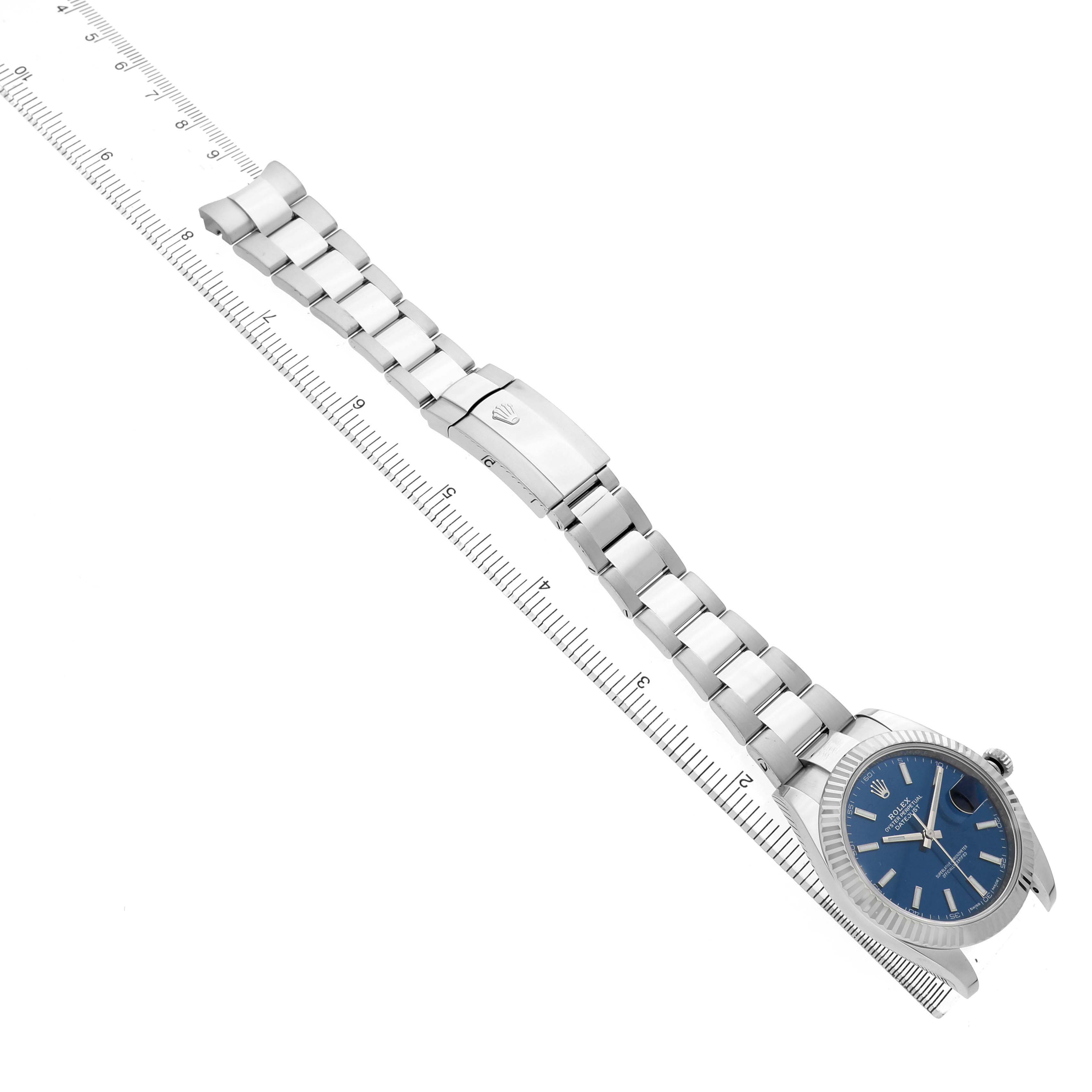 The Rolex Datejust 41 126334 Men's Stainless Steel Blue Dial is shown from a top-down angle, displaying the bracelet, clasp, and watch face against a ruler.