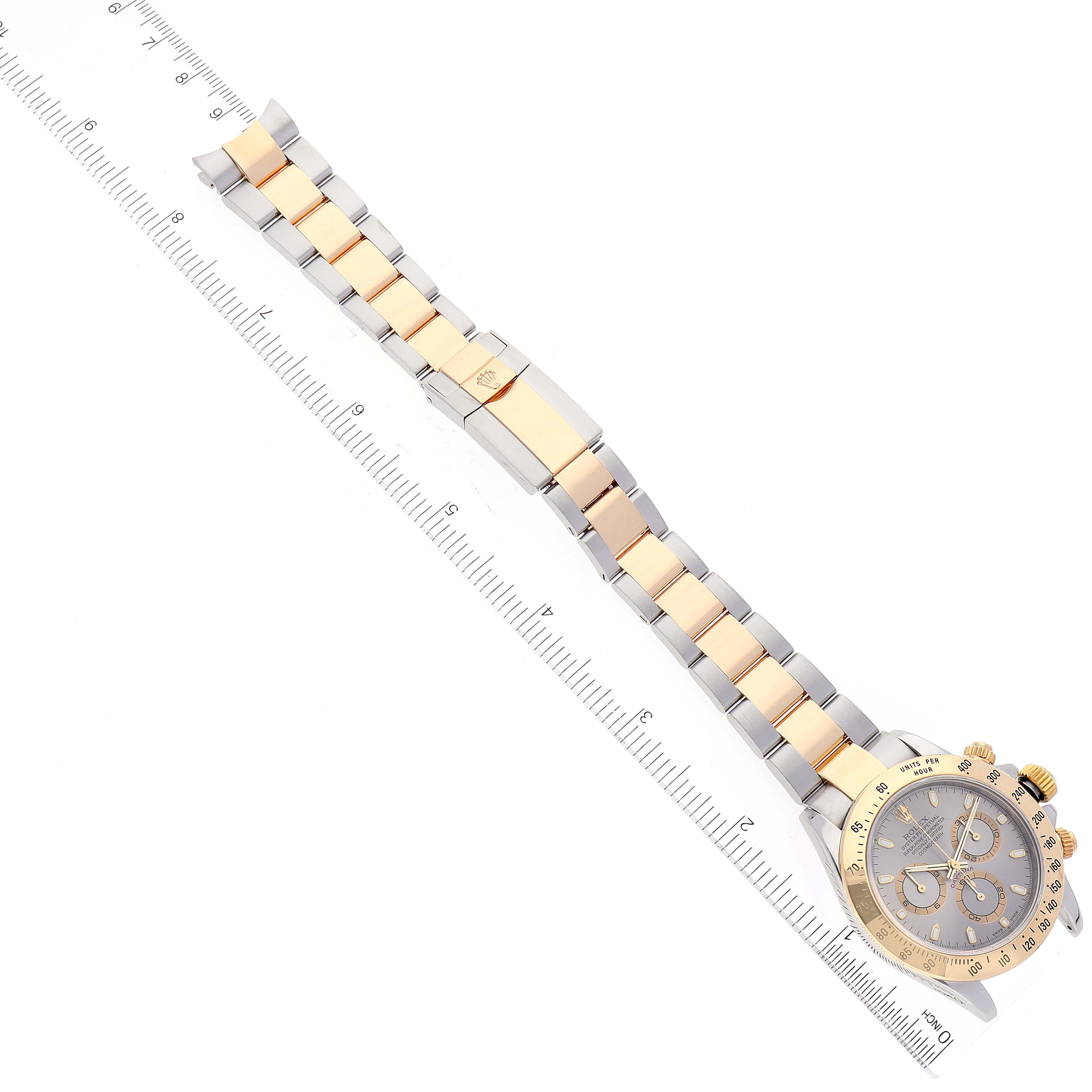 The image shows a Rolex Daytona 116523 Men's Steel and Gold (two tone) Grey Dial 116523 Men's Steel and Gold (two tone) Grey Dial watch laid flat, showcasing its face and two-tone bracelet alongside a ruler.