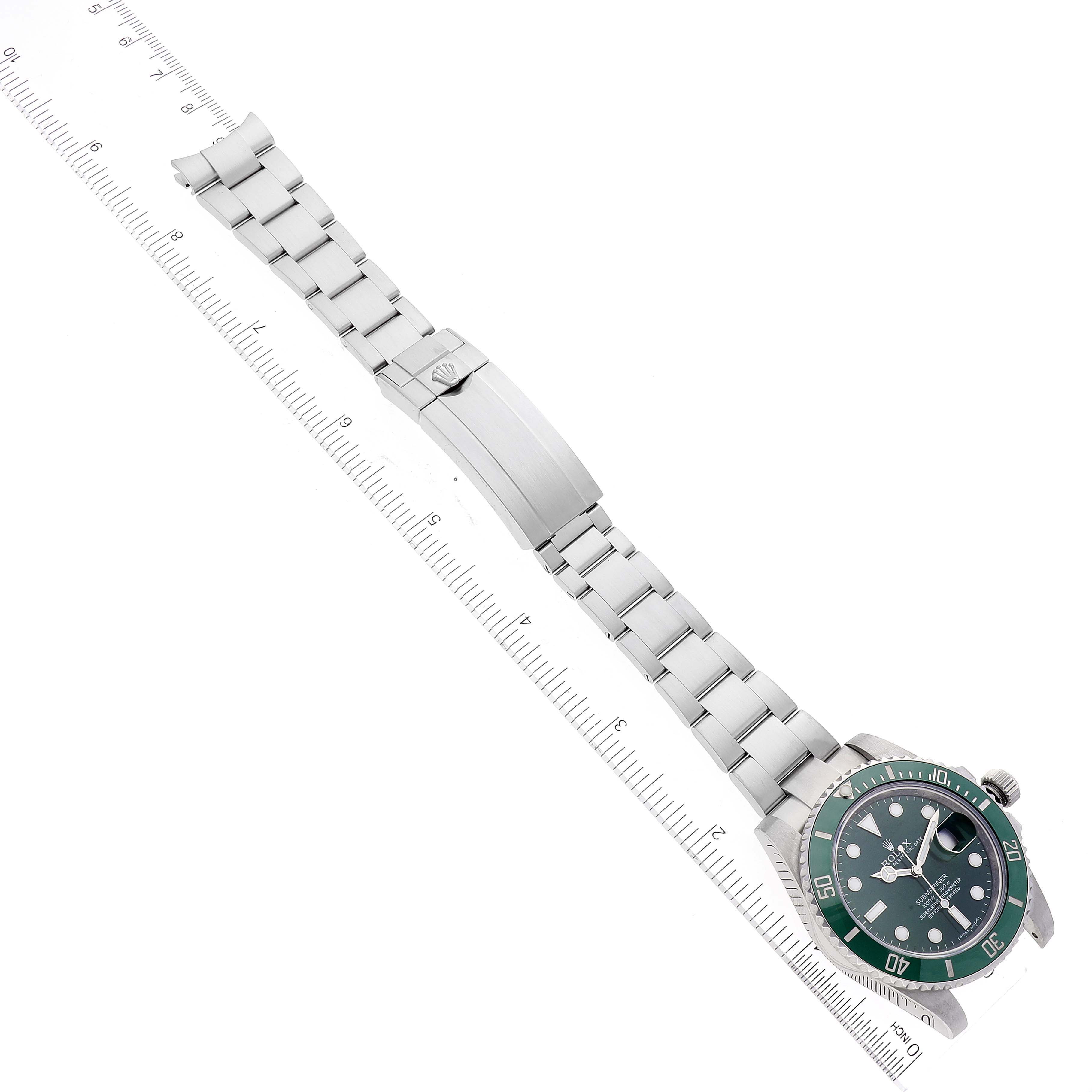 The image shows a top view of a Rolex Submariner 116610LV Men
s Stainless Steel Green Dial 116610LV Men
s Stainless Steel Green Dial watch, displaying the watch face, bezel, and metal bracelet with a measuring ruler beside it.