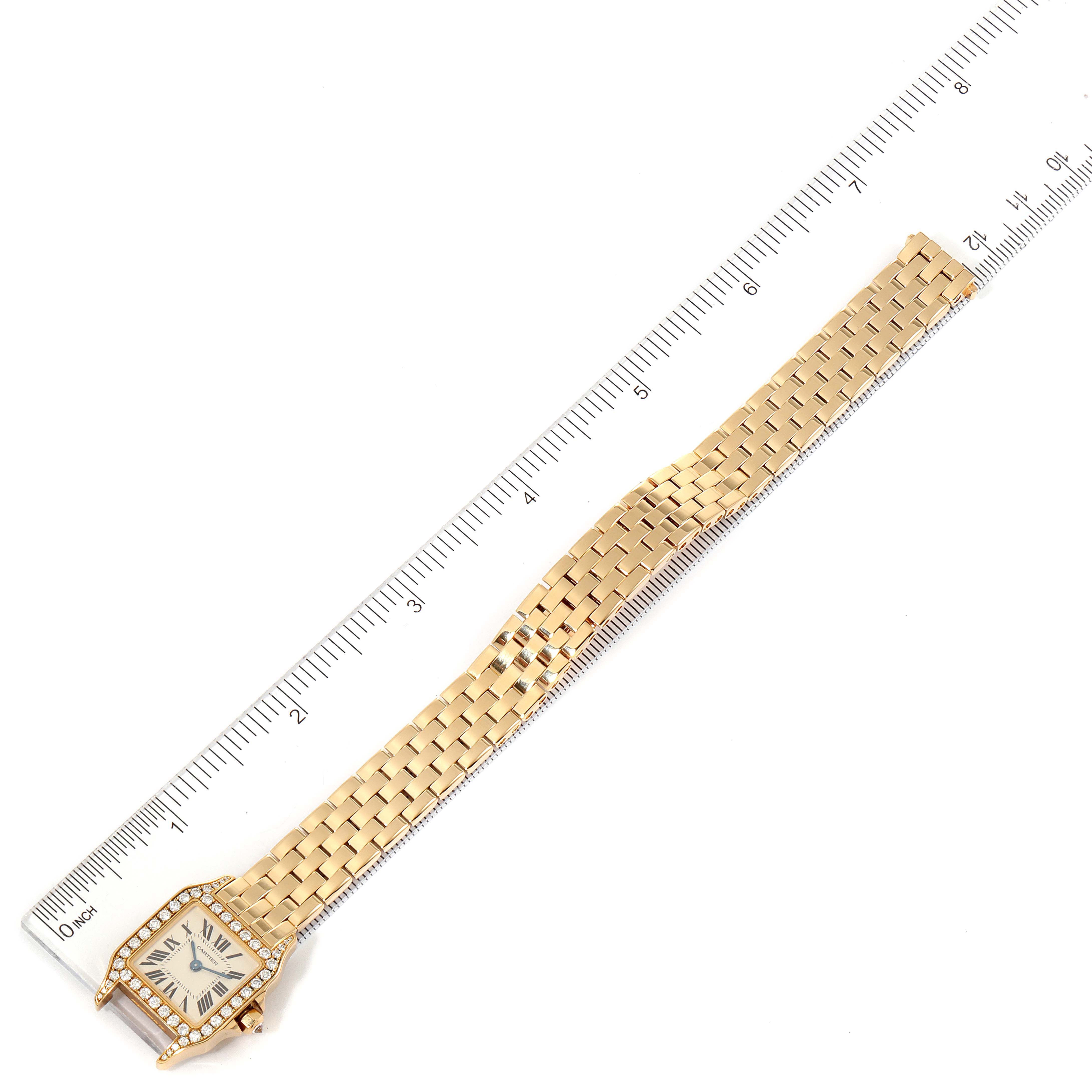 The image shows a Cartier Santos Demoiselle WF9001Y7 Women
s Yellow Gold Silver Dial WF9001Y7 Women
s Yellow Gold Silver Dial watch laid flat with its watch face and gold bracelet visible, alongside a ruler for size reference.