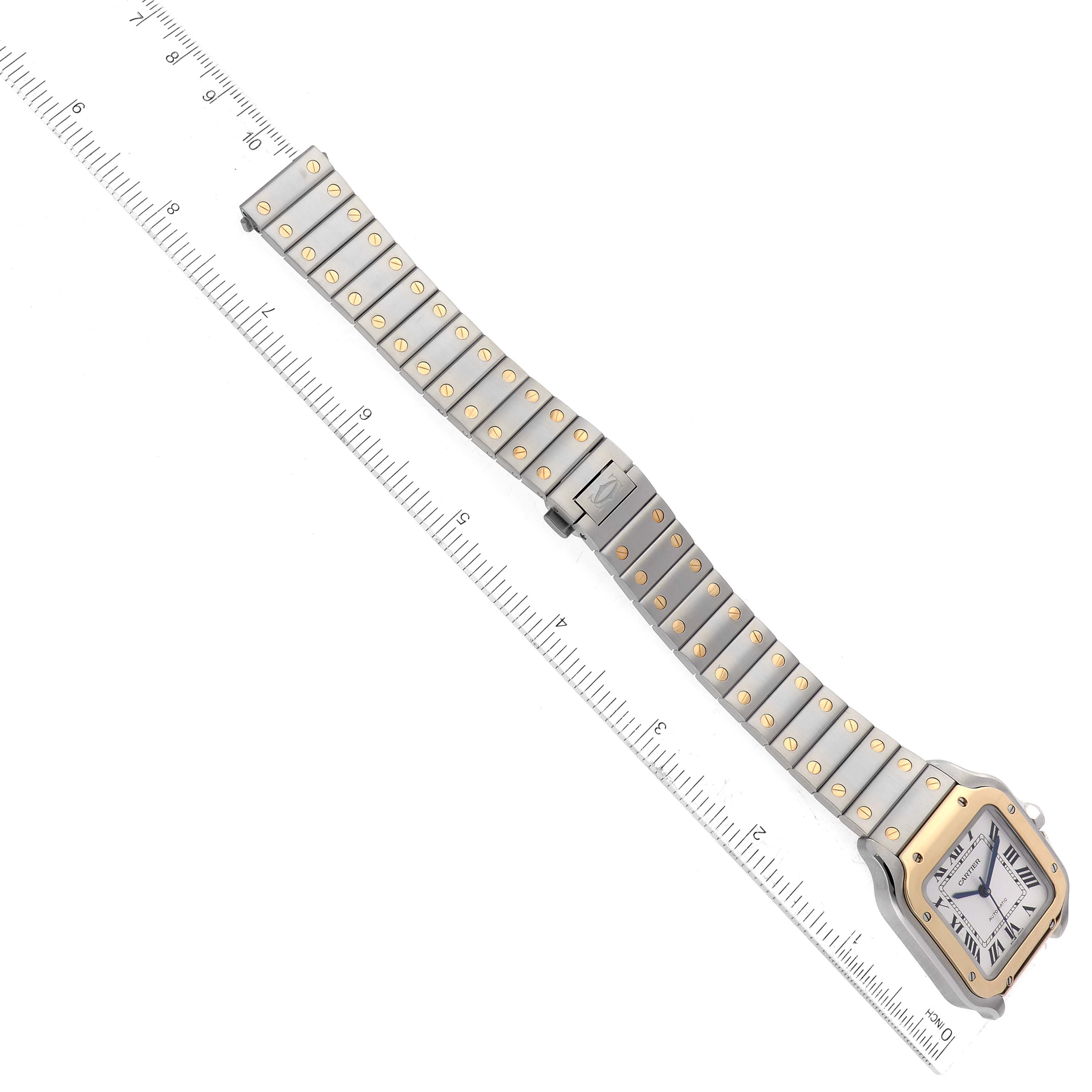 The image shows a bird
s-eye view of a Cartier Santos W2SA0016 Men
s Steel and Gold (two tone) Silver Dial W2SA0016 Men
s Steel and Gold (two tone) Silver Dial watch, displaying its face, band, and a measuring ruler beside it.