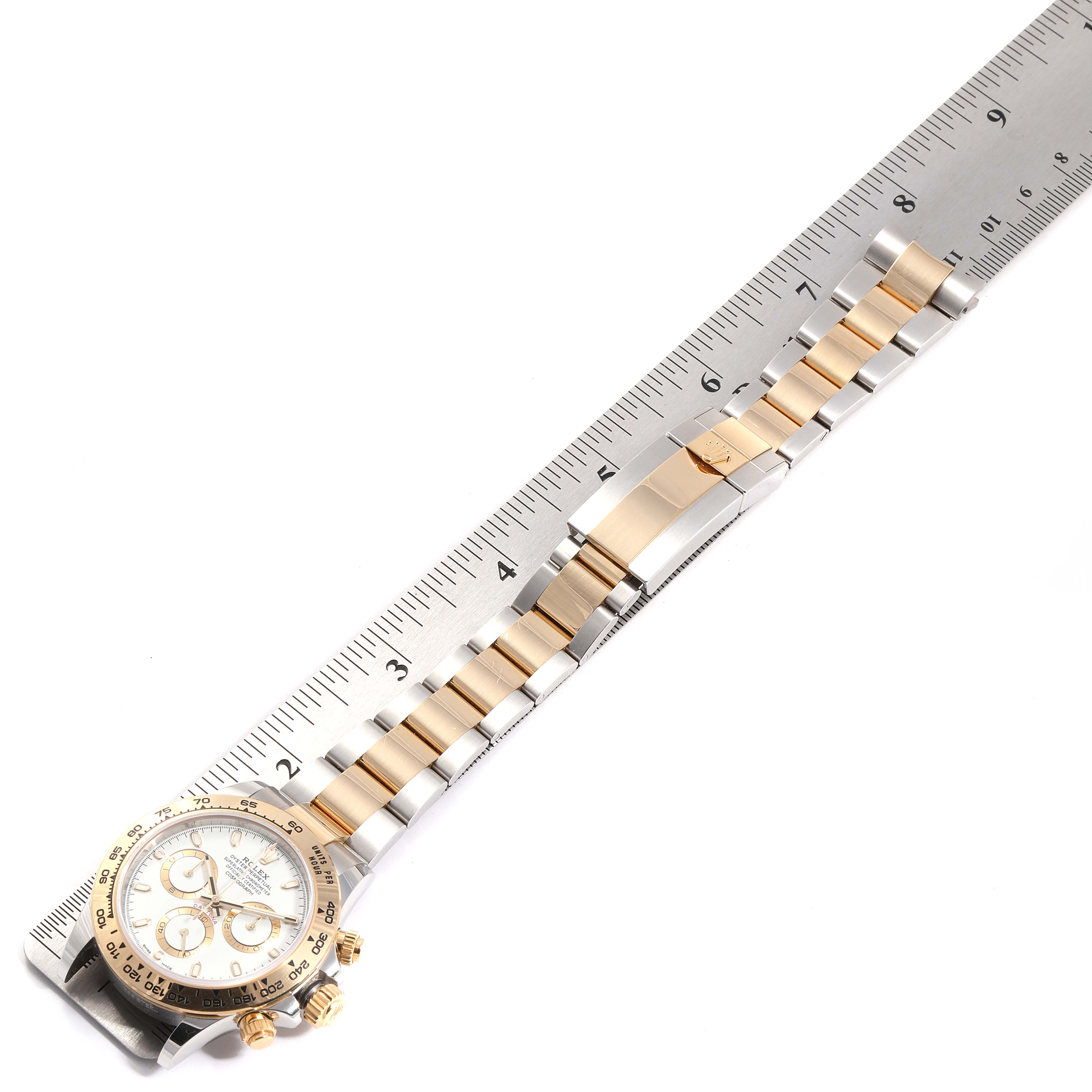 The image shows a Rolex Daytona 116503 Men's Steel and Gold (two tone) White Dial 116503 Men's Steel and Gold (two tone) White Dial watch laid flat on a ruler, displaying its face, bezel, and bracelet from an overhead angle.