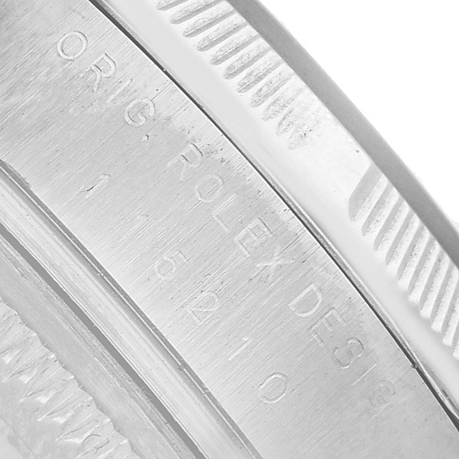 The image shows a close-up of the side casing, bezel, and engraved branding of a Rolex Date 115210 Men's Stainless Steel White Dial watch.