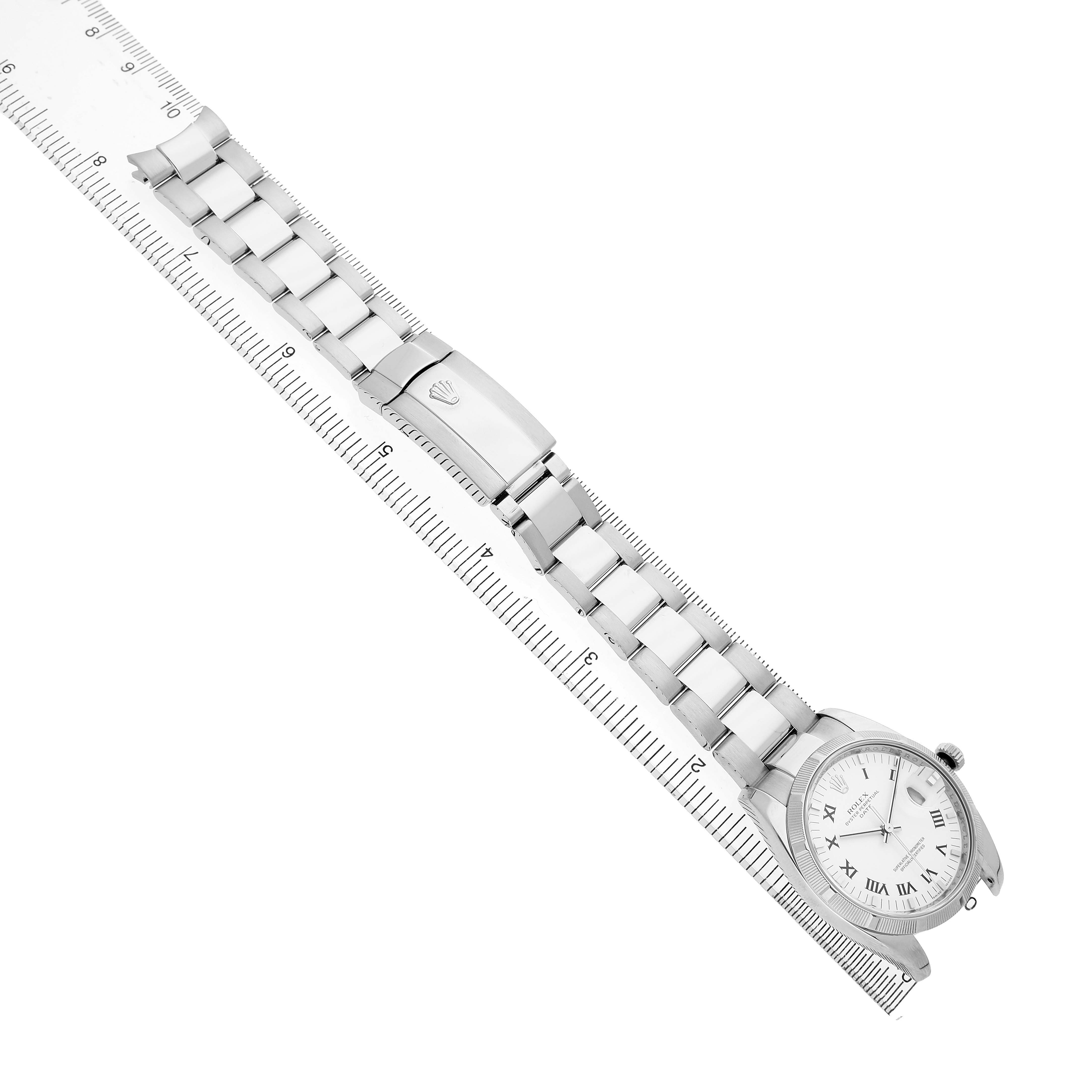 The Rolex Date 115210 Men's Stainless Steel White Dial watch is shown at an angle displaying its full bracelet, clasp, and dial, aligned beside a ruler.