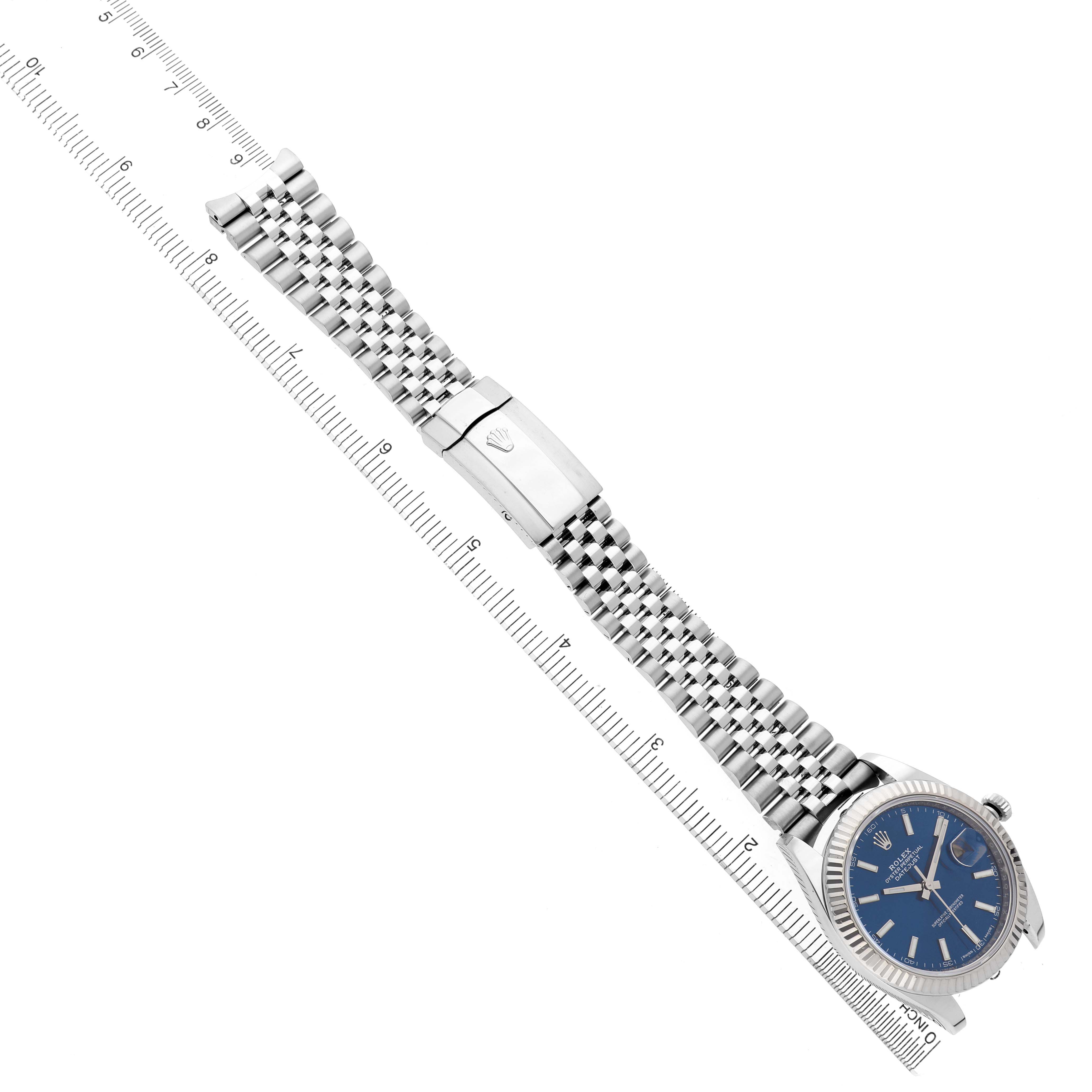 The Rolex Datejust 41 126334 Men's Stainless Steel Blue Dial watch is shown from an angled, top-down view, highlighting the bracelet and clasp against a ruler.