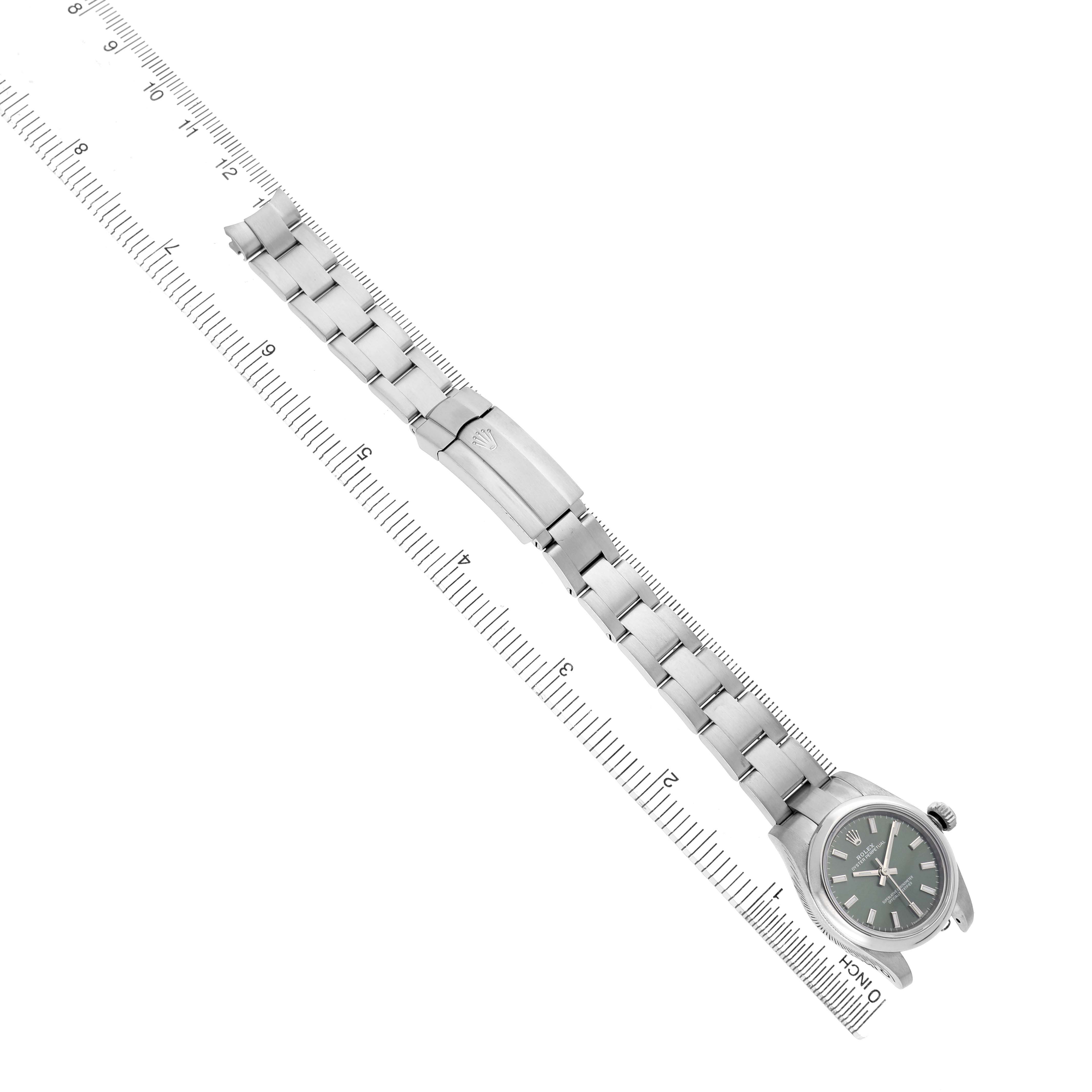 The Rolex Oyster Perpetual 176200 Women's Stainless Steel Green Dial watch is shown from an overhead angle, highlighting its bracelet and clasp alongside a ruler for scale.