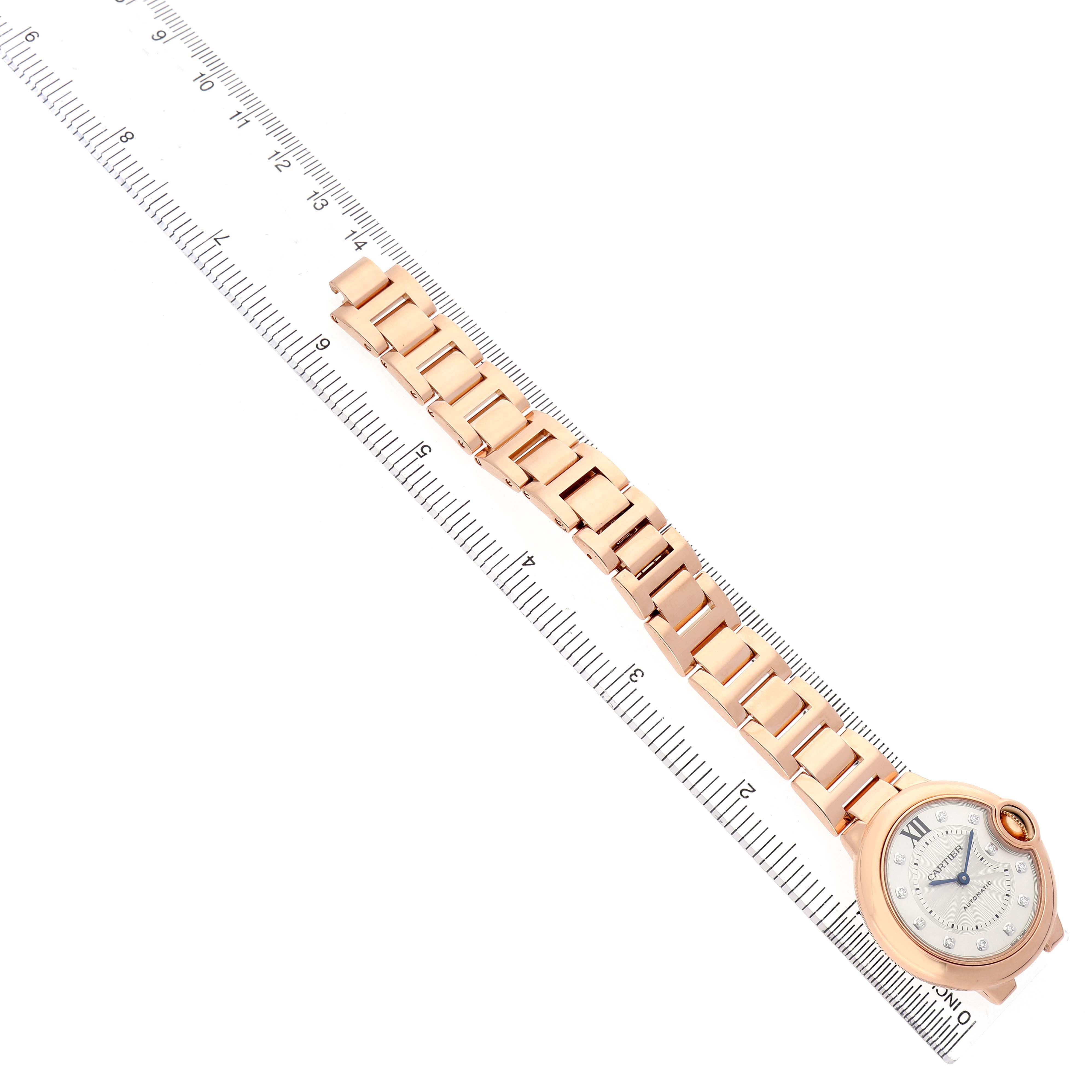 The Cartier Ballon Bleu WE902034 Women's Rose Gold Silver Dial watch is shown from a top-down angle, displaying its bracelet and face alongside a measuring ruler.