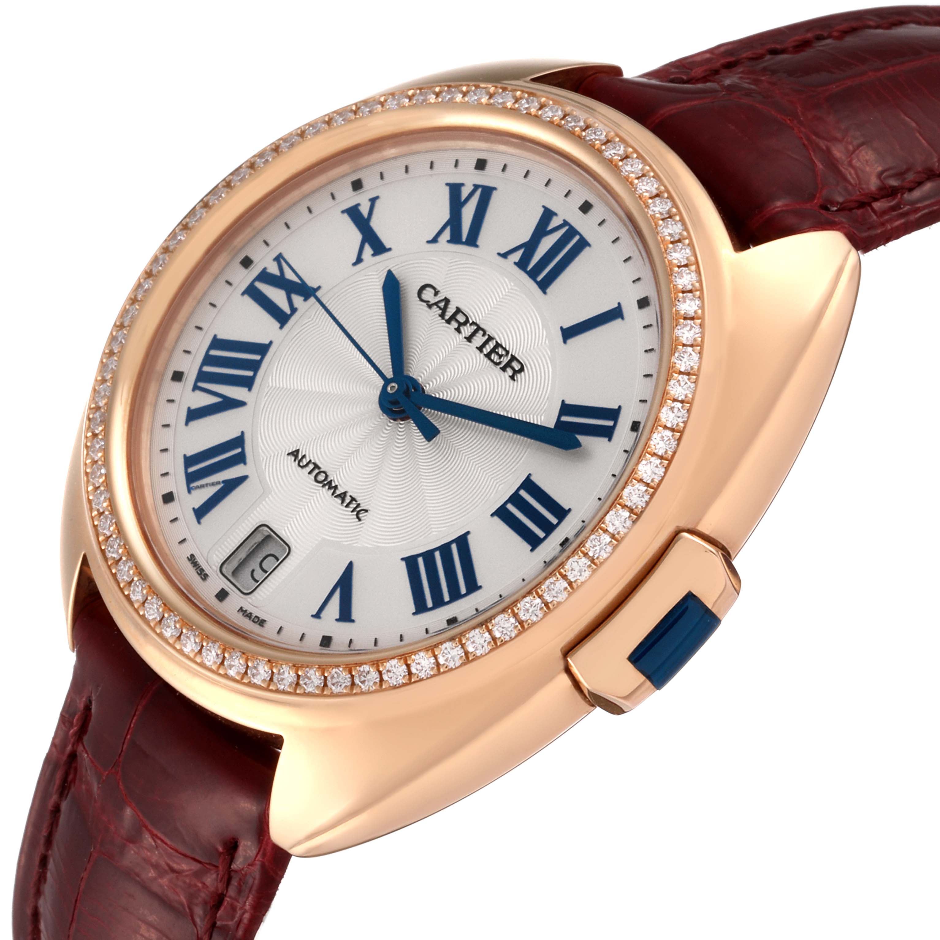 The Cartier Clé watch is shown at an angle that highlights its face, bezel studded with diamonds, and burgundy leather strap.