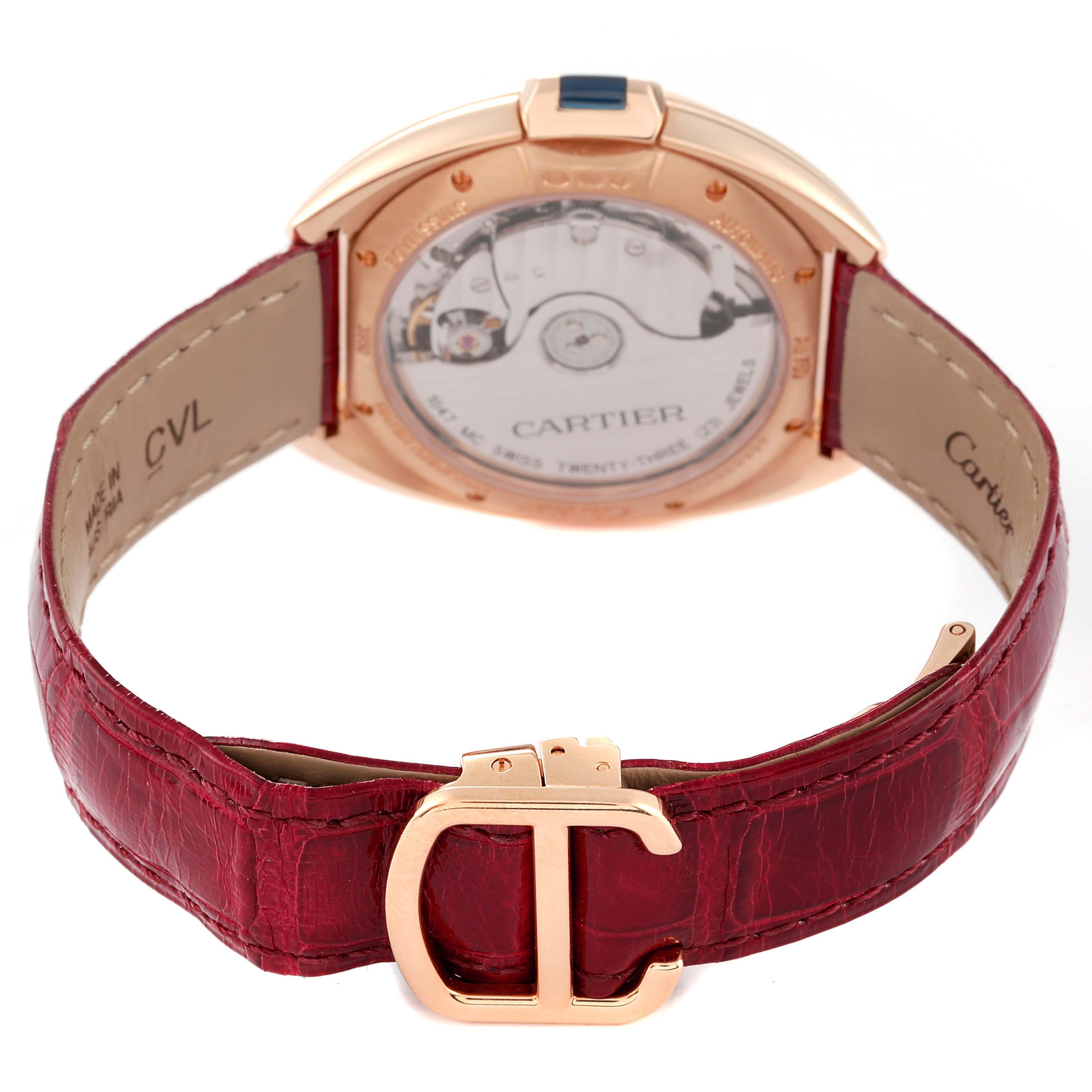 The image shows the back of a Cartier Clé watch, highlighting its movement, case, red leather strap, and gold buckle.