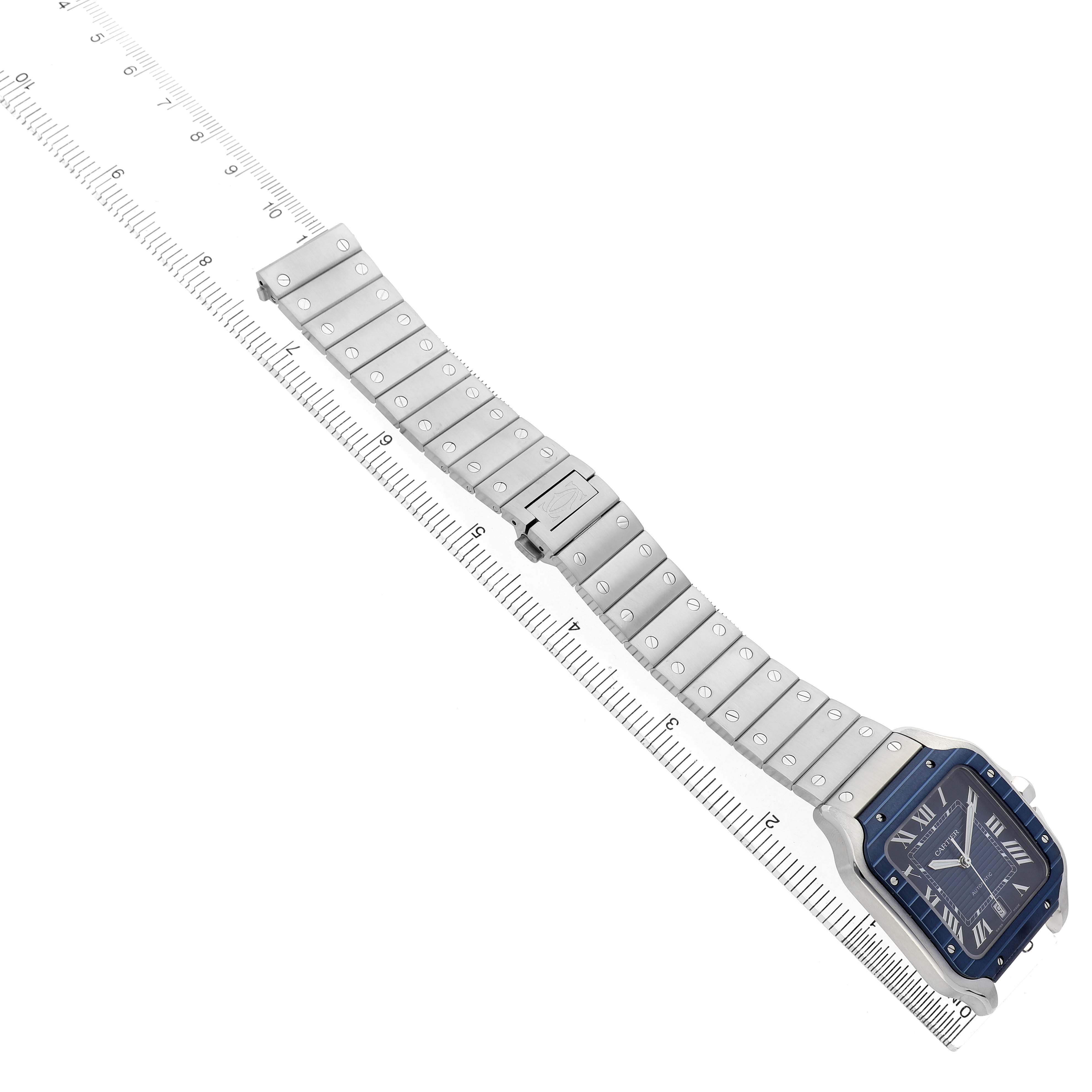 The Cartier Santos WSSA0048 Men's Stainless Steel Blue Dial watch is shown from a slightly elevated angle, displaying its face and full bracelet alongside a ruler.