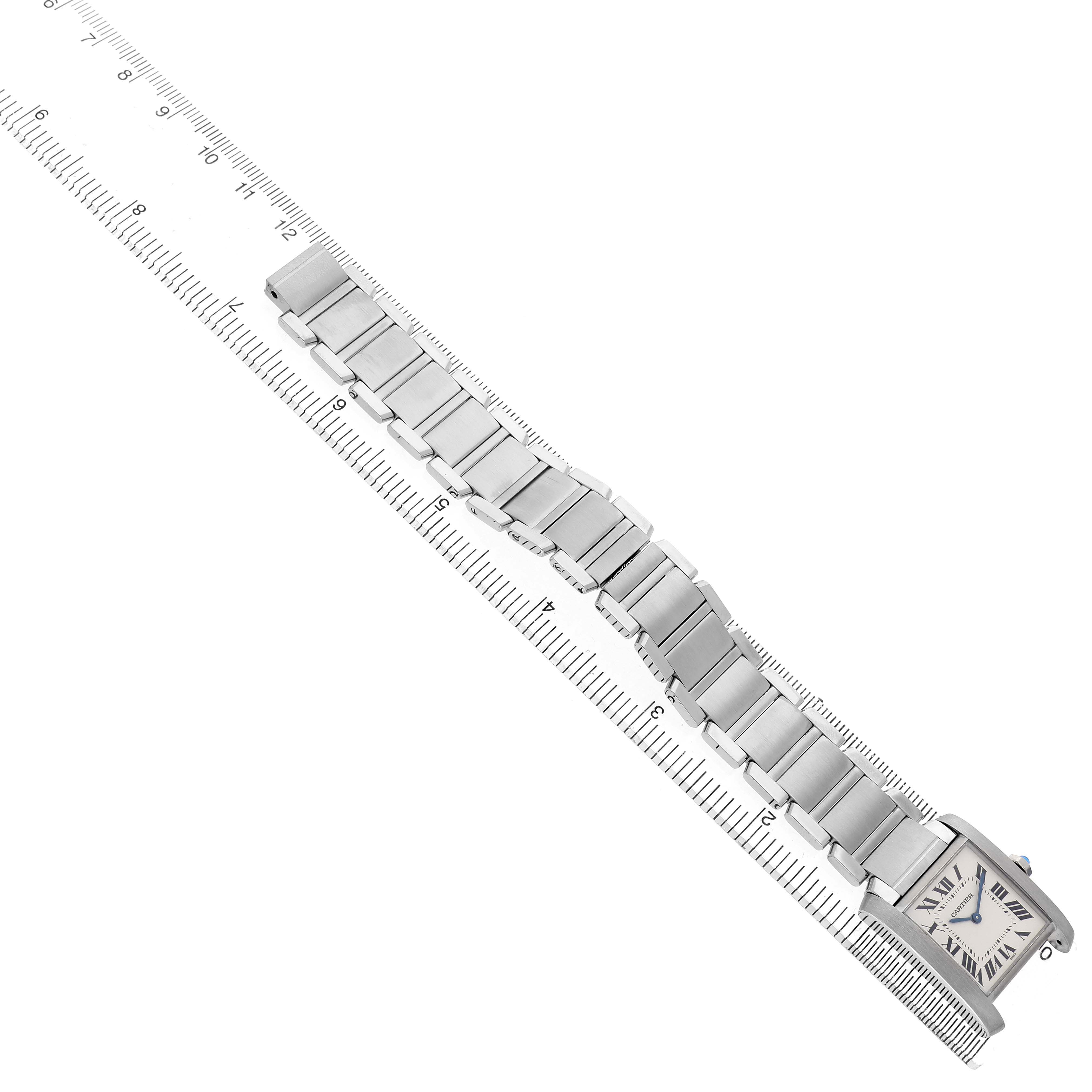 The Cartier Tank Française watch is shown from a top view, highlighting its face and metal bracelet against a ruler.