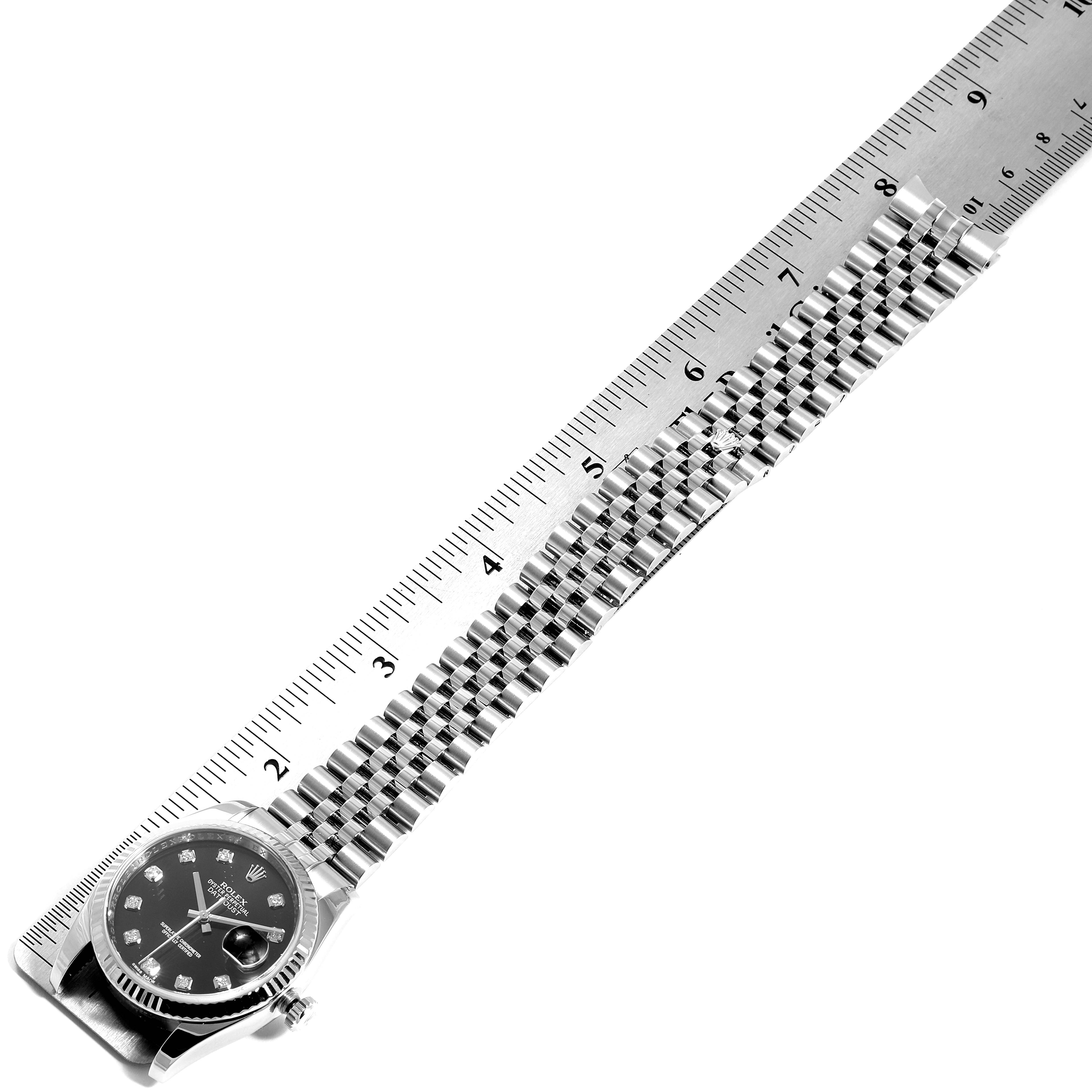 The Rolex Datejust 116234 Men's Stainless Steel Black Dial 116234 Men's Stainless Steel Black Dial watch is laid flat with its band extended alongside a ruler, showing its length.