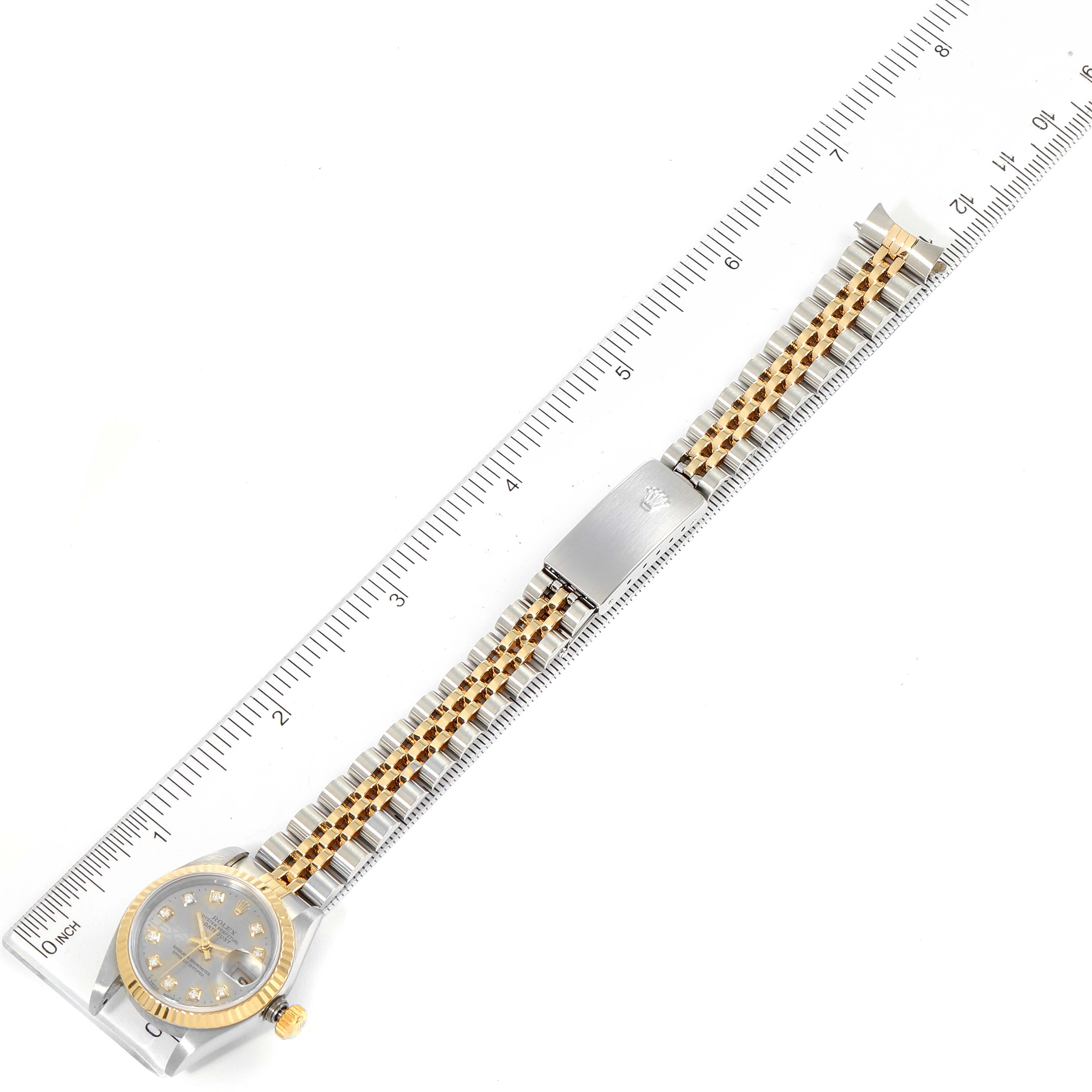 This image shows the top view of a Rolex Datejust 79173 Women
s Steel and Gold (two tone) Grey Dial 79173 Women
s Steel and Gold (two tone) Grey Dial watch with a two-tone band and a measuring scale beside it.