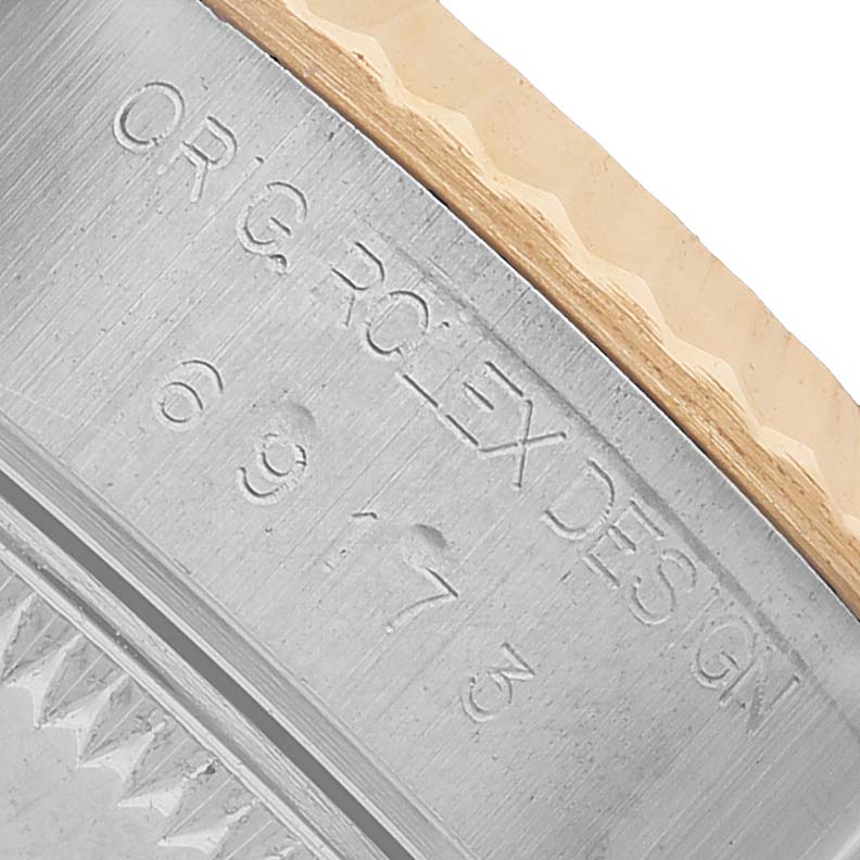 The image shows a close-up of the engraved side of a Rolex Datejust 79173 Women's Steel and Gold (two tone) White Dial bezel with visible text and design.