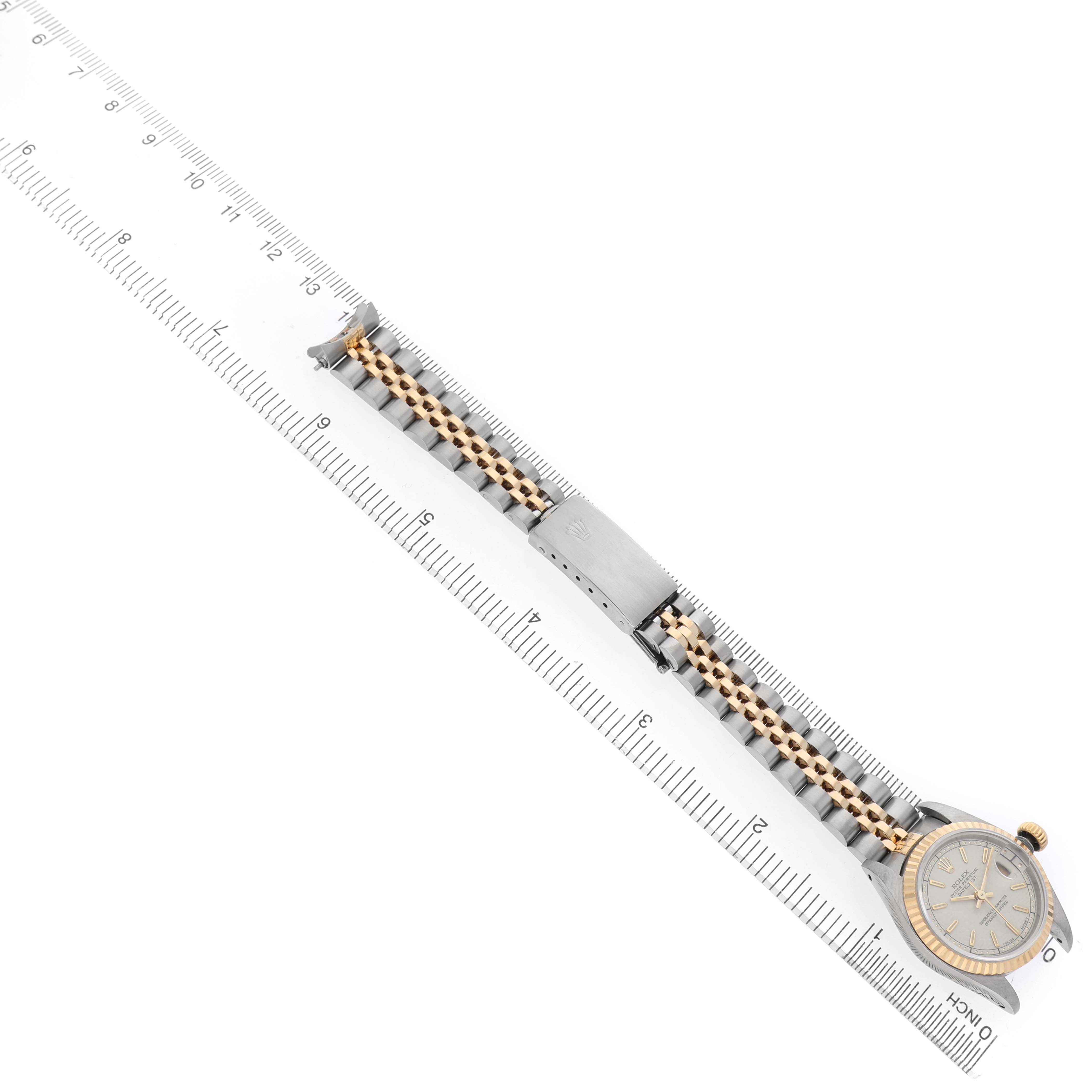 The image shows a Rolex Datejust 69173 Women's Stainless Steel White Dial watch positioned diagonally next to a ruler, highlighting the bracelet and case from a top view.