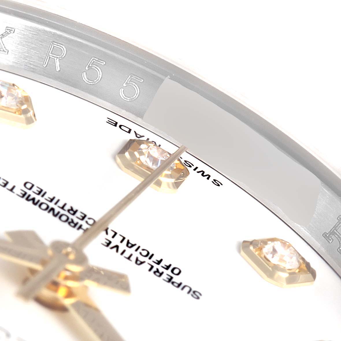 The close-up image of the Rolex Datejust 116243 Men's Steel and Gold (two tone) White Dial 116243 Men's Steel and Gold (two tone) White Dial watch shows part of the dial, gems, hands, and inner bezel with engravings.