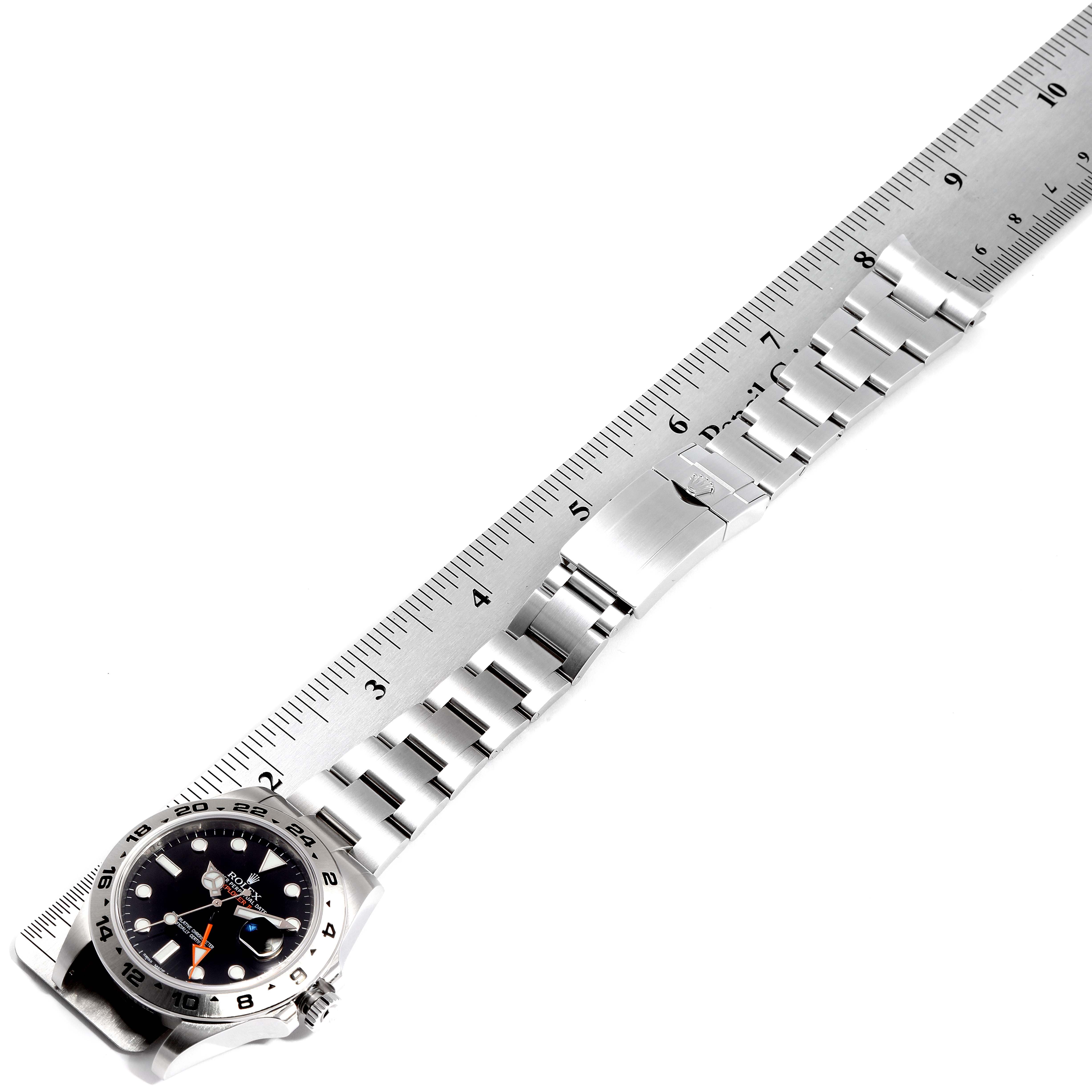The image shows a top-down view of a Rolex Explorer 216570 Men
s Stainless Steel Black Dial 216570 Men
s Stainless Steel Black Dial watch with its bracelet, clasp, and part of the dial alongside a ruler for scale.