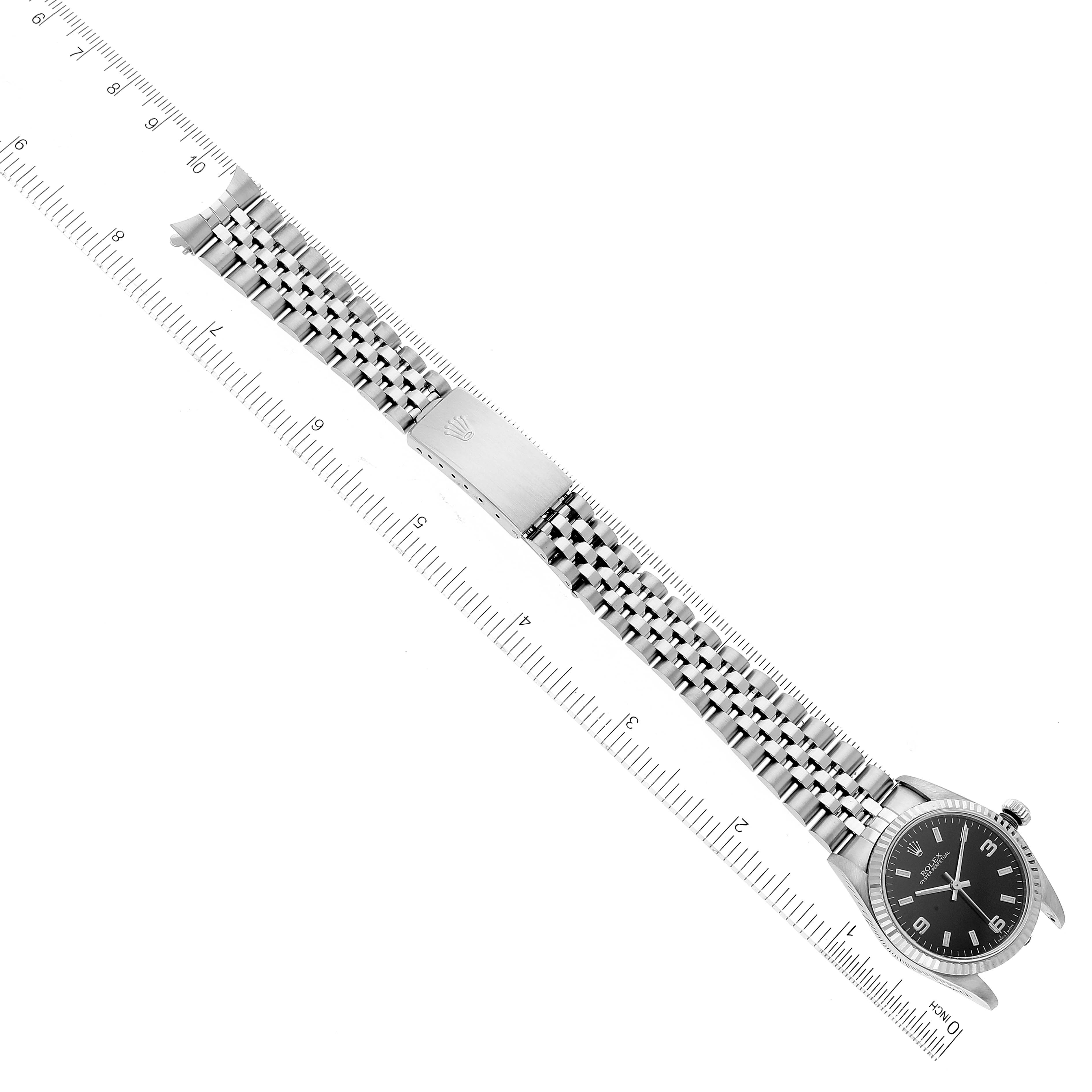 The image shows a top-down view of the Rolex Mid-Size 77014 Women's Stainless Steel Black Dial 77014 Women's Stainless Steel Black Dial watch, focusing on its face, bezel, and bracelet with measuring rulers.