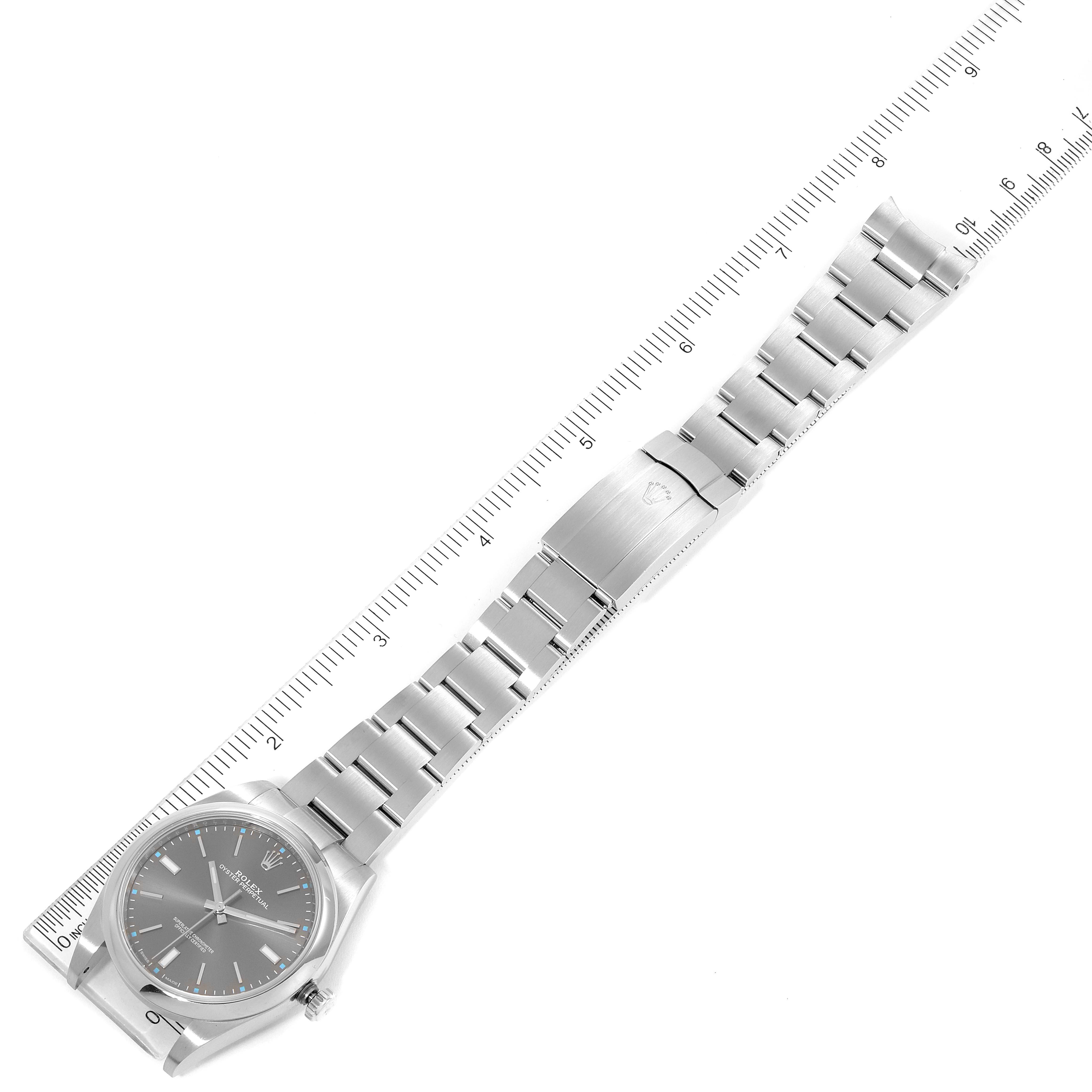 The image shows an aerial view of a Rolex Oyster Perpetual 114300 Men's Stainless Steel Silver Dial 114300 Men's Stainless Steel Silver Dial watch, including its face, bracelet, and clasp next to a ruler for scale.
