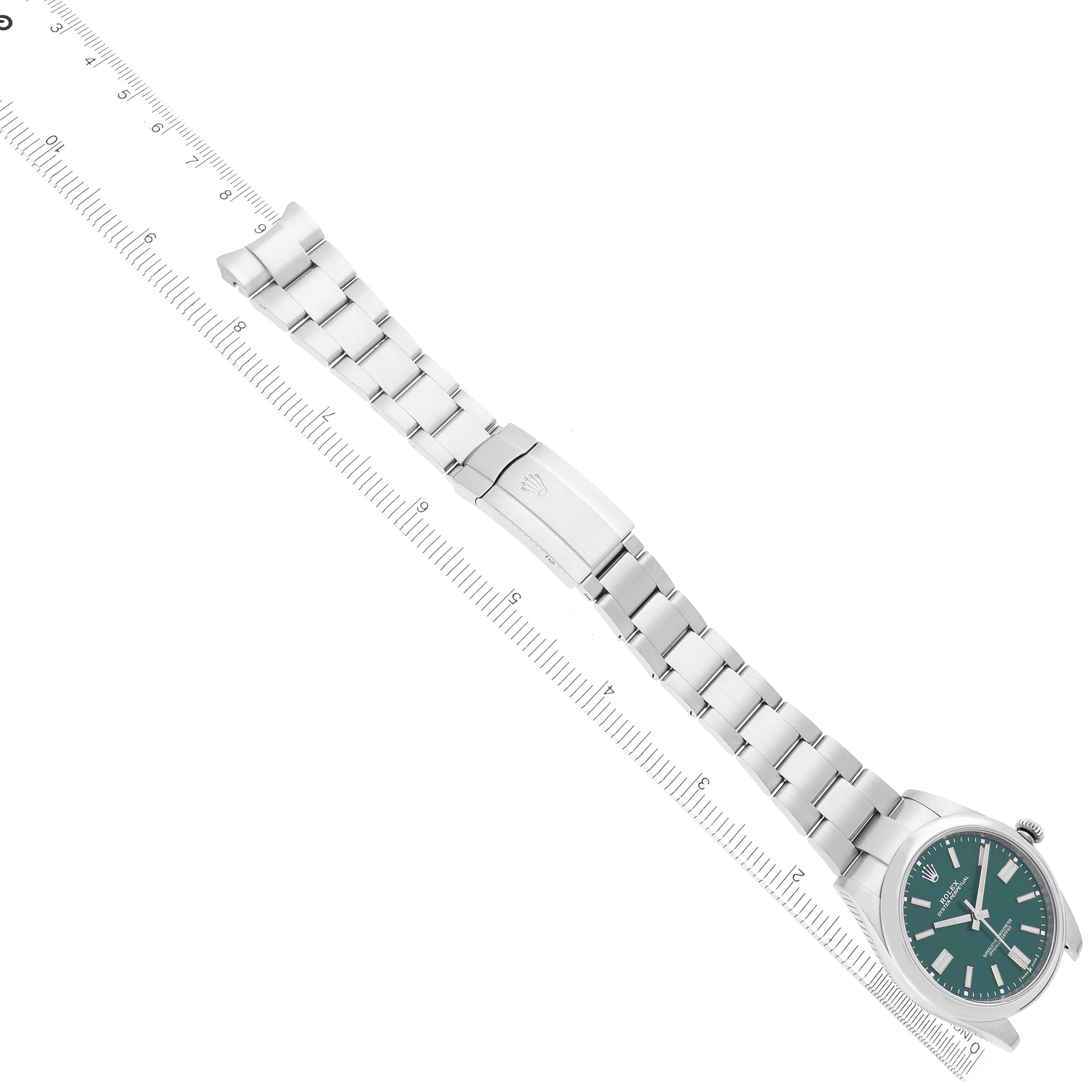 The Rolex Oyster Perpetual model 124300 watch is shown from an angled top view, displaying the face, bracelet, and clasp arrangement alongside a ruler for scale.