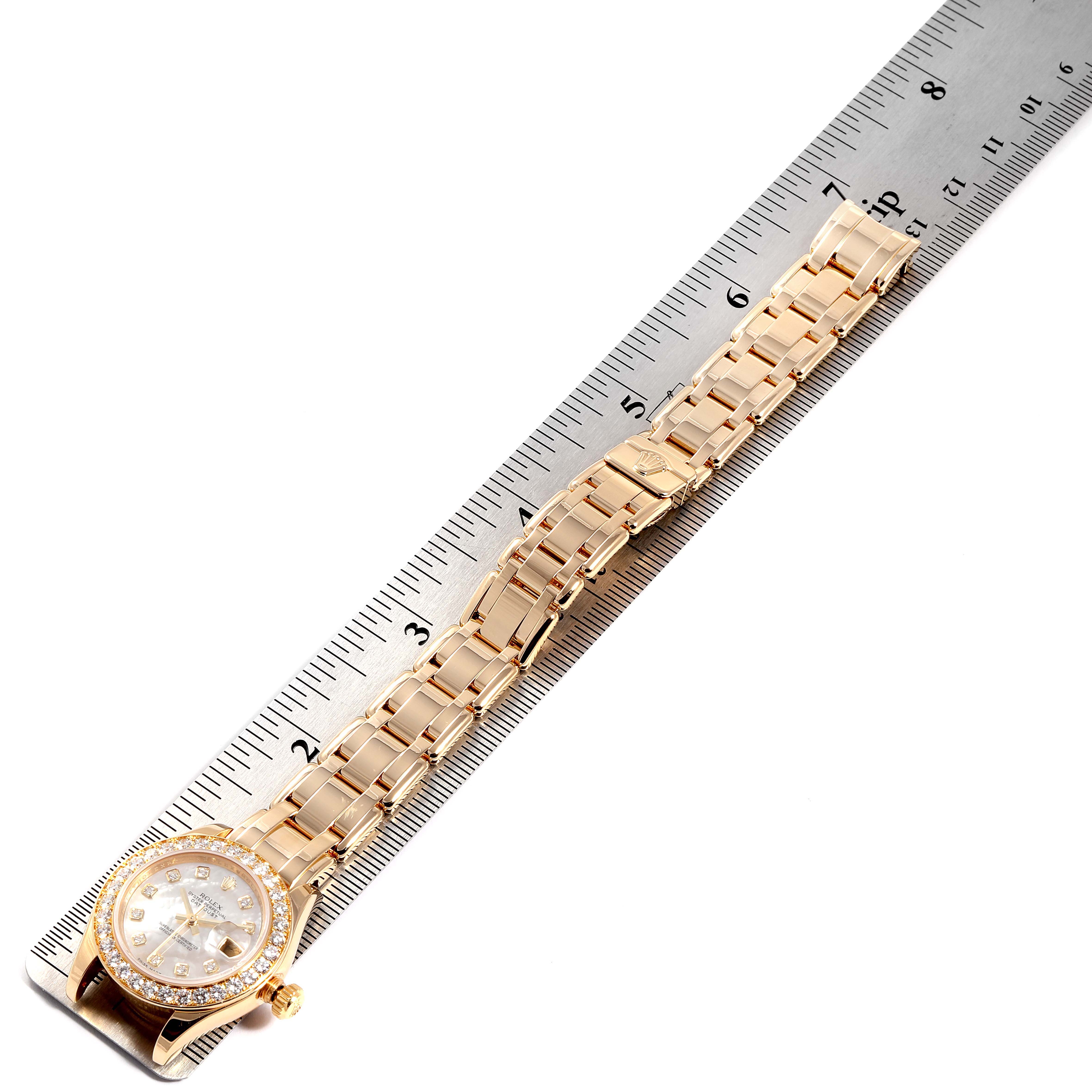 The Rolex Pearlmaster 80298 Women
s Yellow Gold Mother of Pearl Dial 80298 Women
s Yellow Gold Mother of Pearl Dial watch is shown from a top-down angle, including the entire bracelet and the watch face, with a ruler for scale.