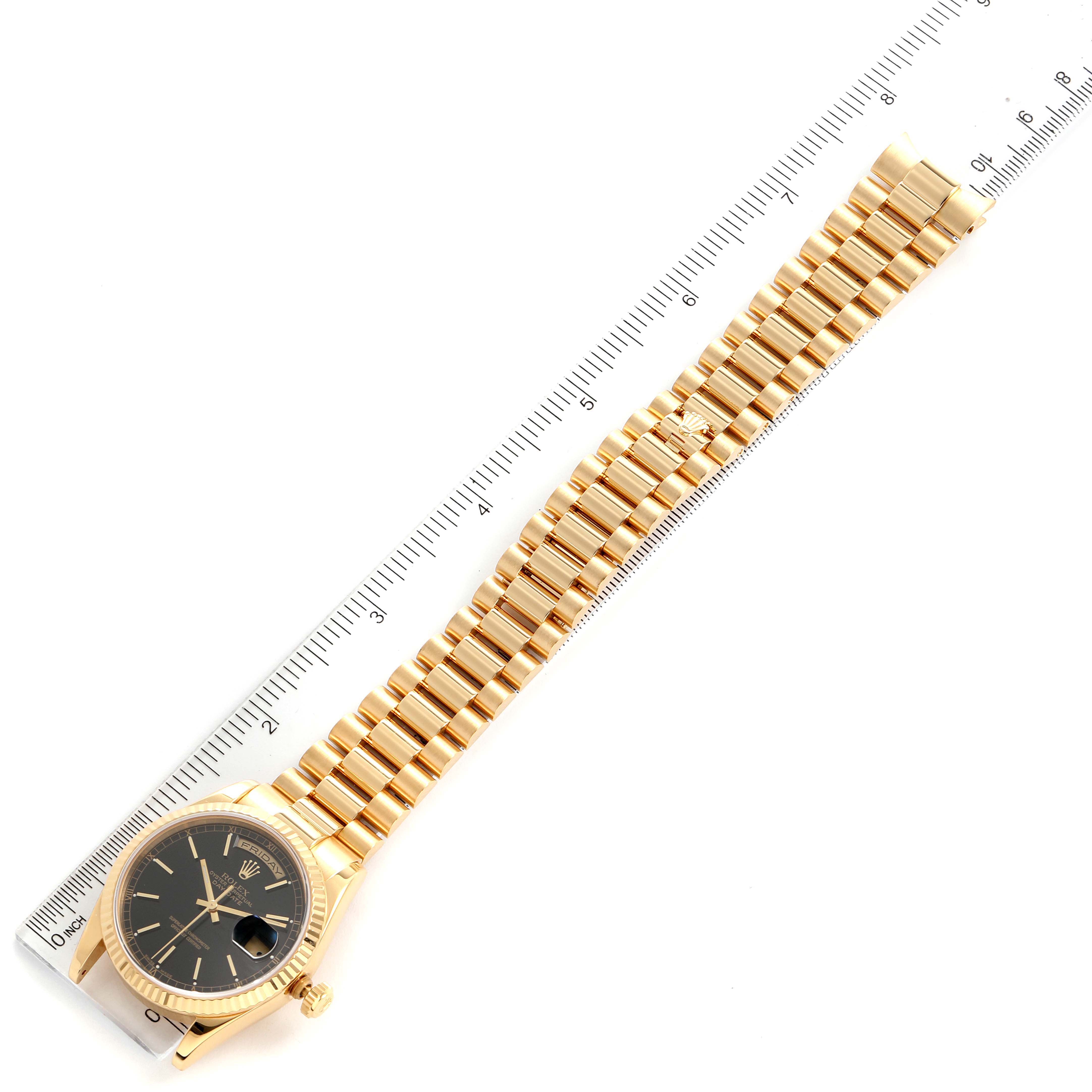 This image shows the Rolex President 118238 Men
s Yellow Gold Black Dial 118238 Men
s Yellow Gold Black Dial model watch laid flat, featuring its full bracelet and ruler for scale.