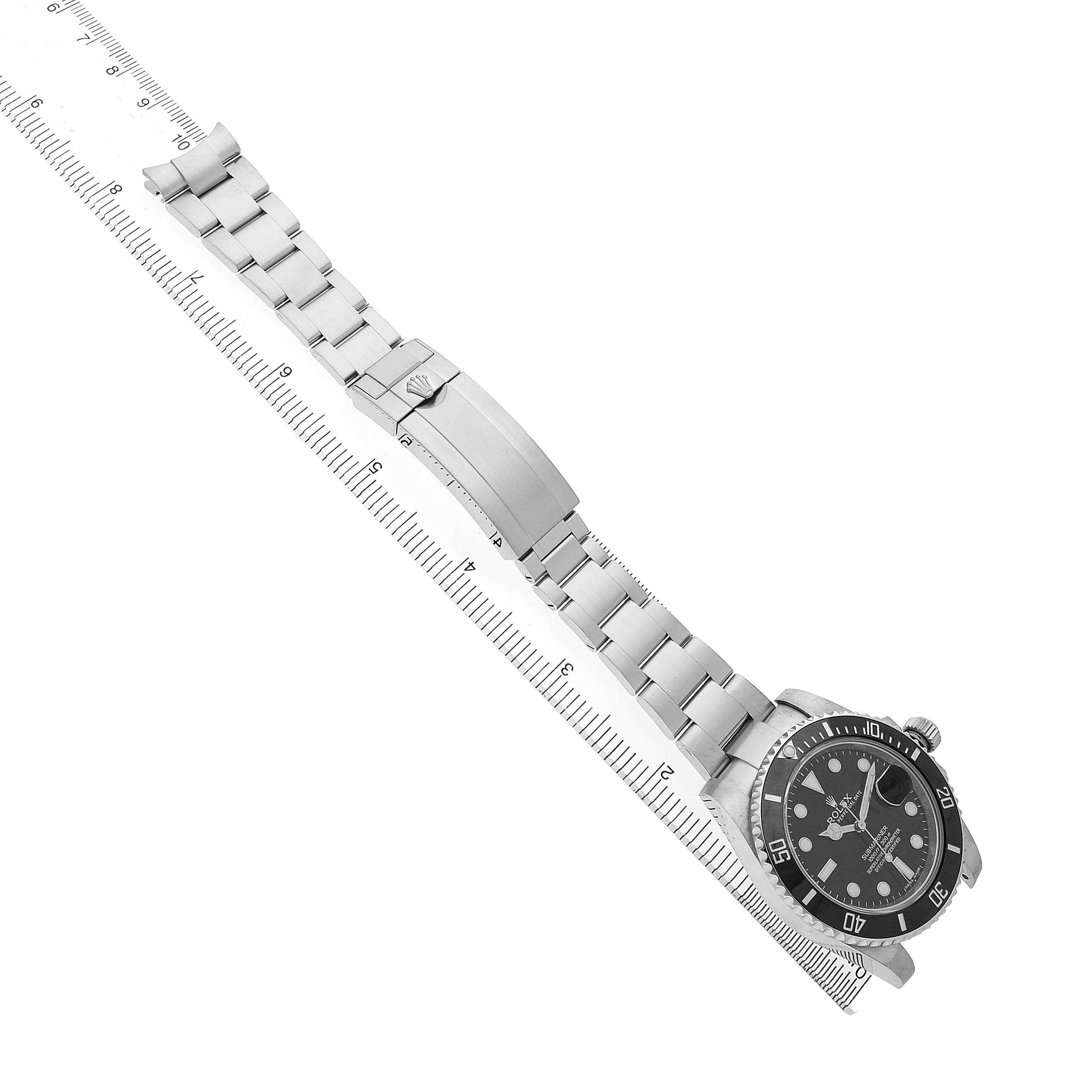 The Rolex Submariner M116610LN-0001 Men's Stainless Steel Black Dial watch is shown at an angle, displaying the bracelet, clasp, and face, with a ruler underneath for scale.