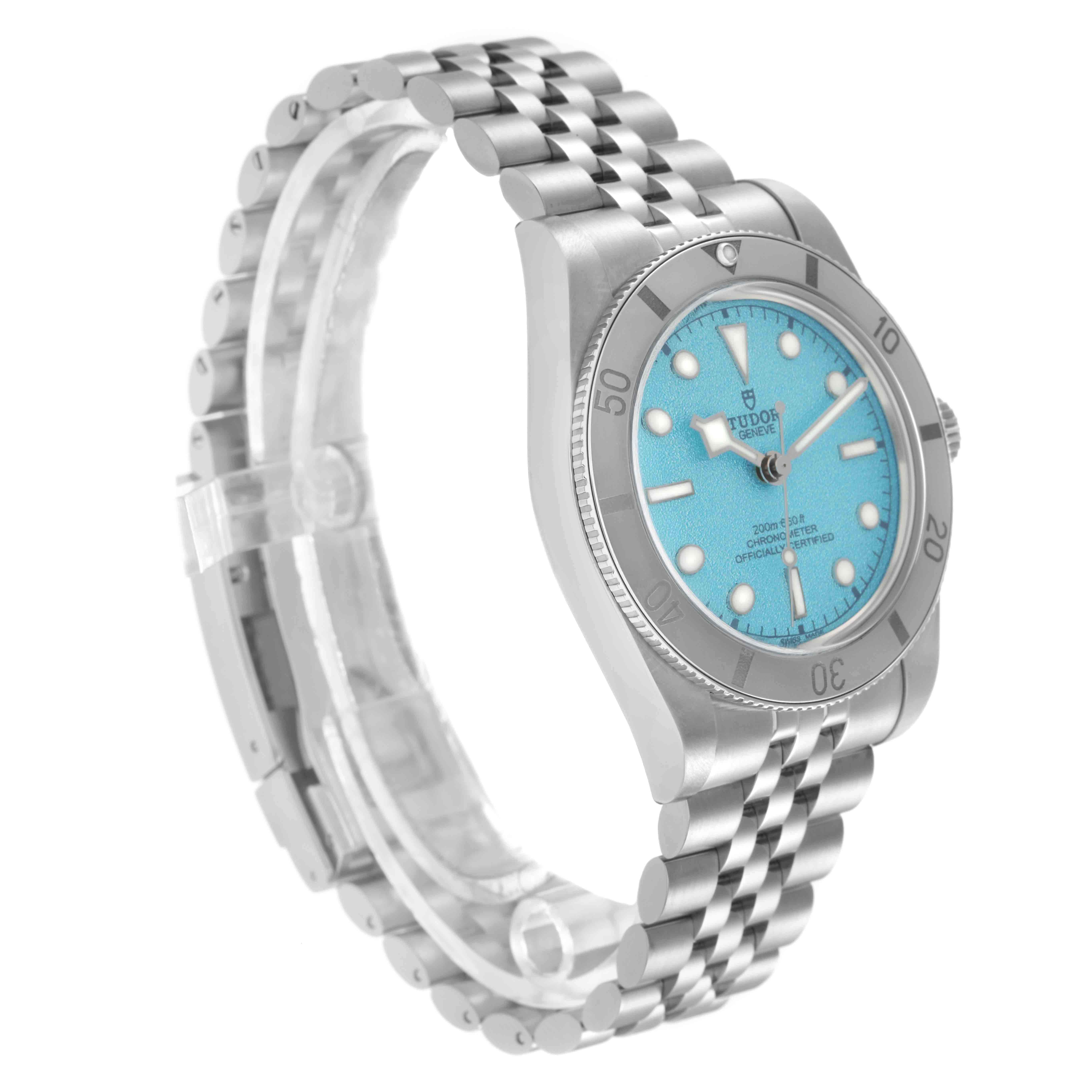 The Tudor Heritage Black Bay model 79000 is shown at a three-quarter angle, highlighting the bezel, cyan dial, crown, and stainless steel bracelet.