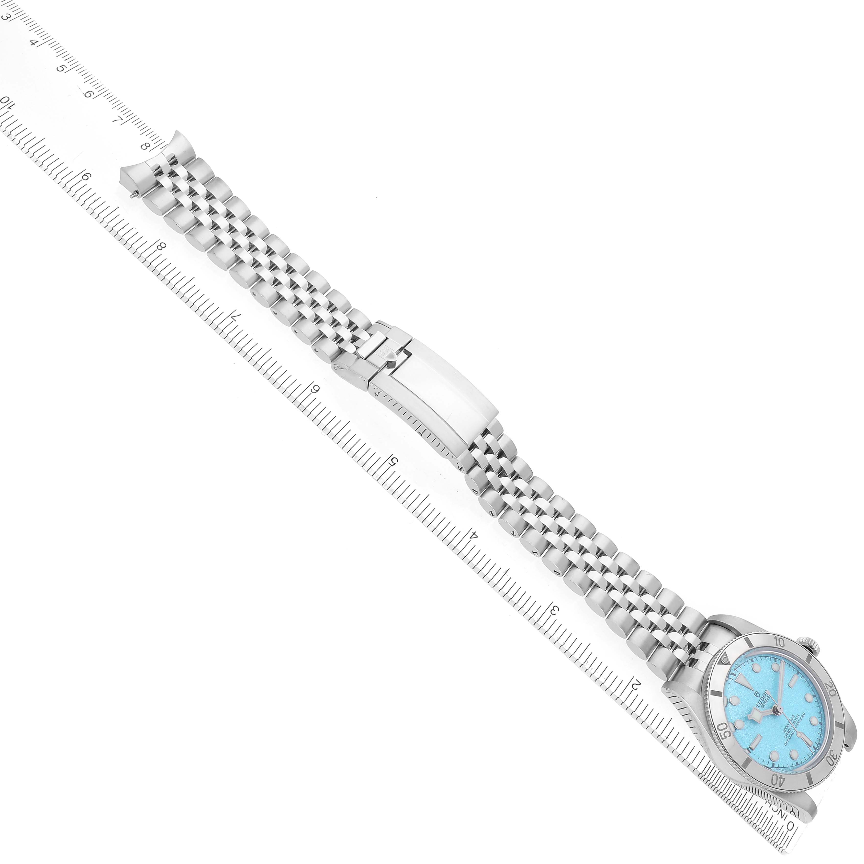 The Tudor Heritage Black Bay model 79000 watch is shown from a top-down angle, featuring the watch face and full metal bracelet extended alongside a ruler.