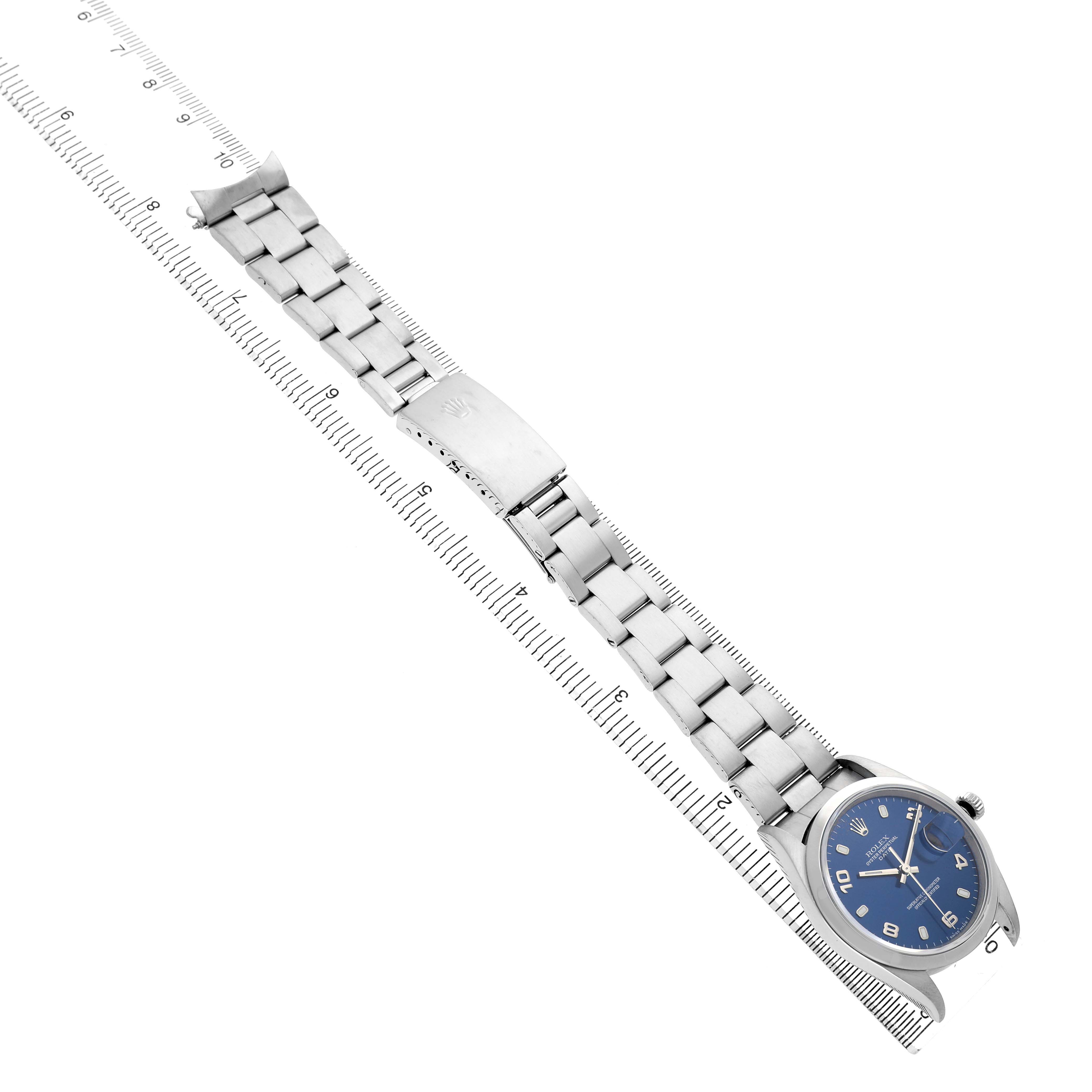 The Rolex Date 15200 Men's Stainless Steel Blue Dial watch is positioned diagonally, showing the face, band, and clasp with a ruler for scale.