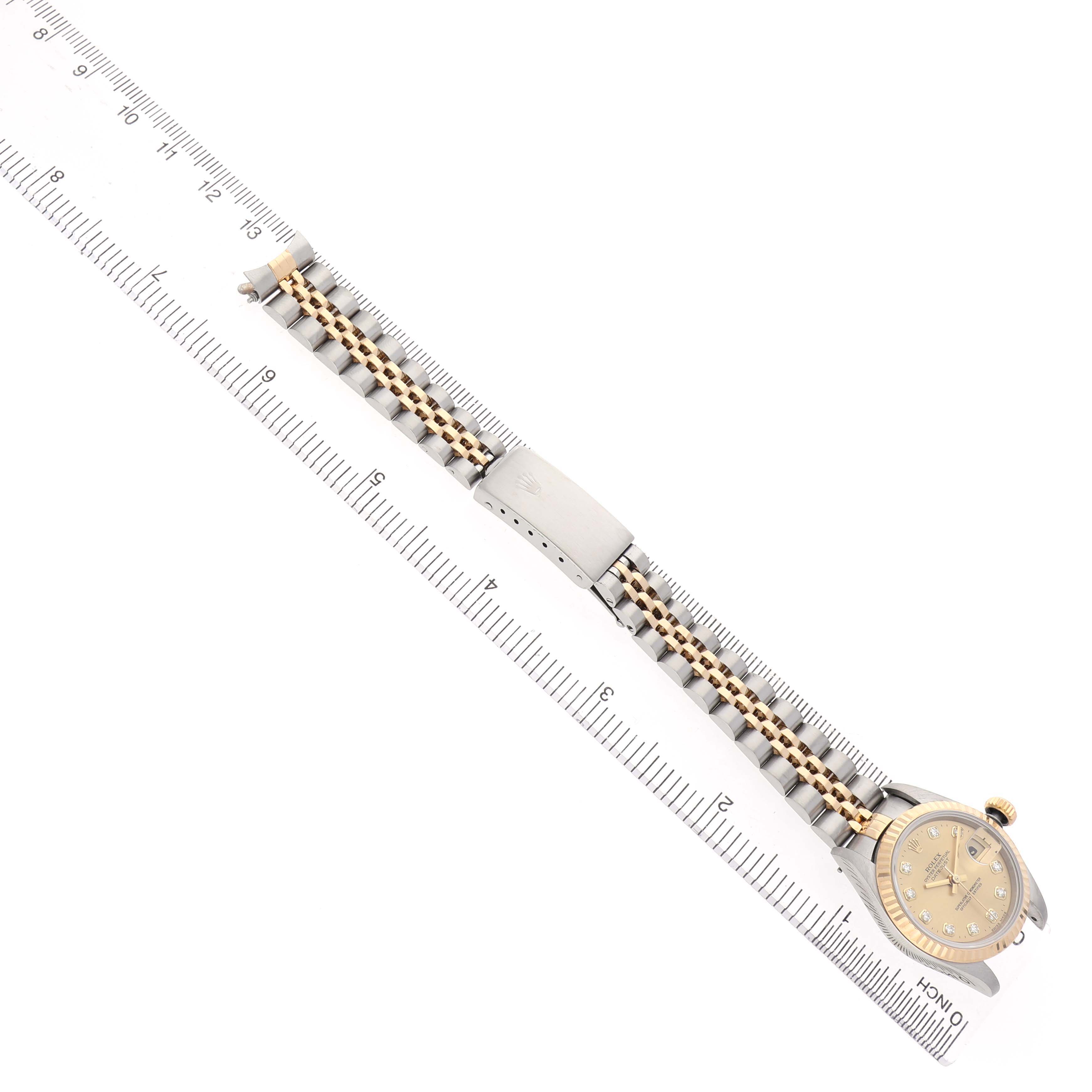 The Rolex Datejust 69173 Women's Steel and Gold (two tone) Champagne Dial watch is shown diagonally with its face, band, and clasp visible, placed next to a ruler.