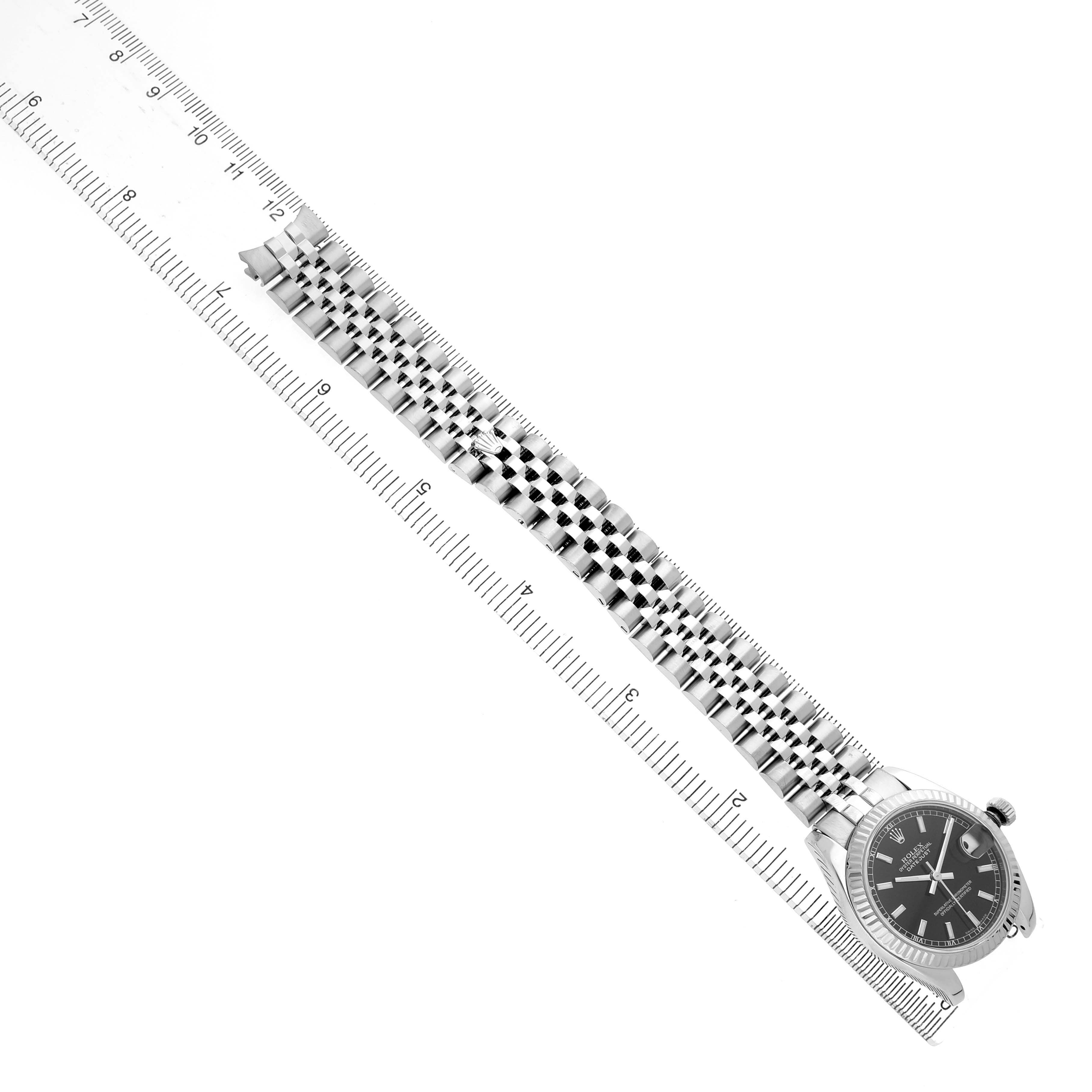 The Rolex Mid-Size 178274 Women's Stainless Steel Black Dial watch is shown in a top-down view, displaying the face, case, and extended bracelet alongside a ruler.