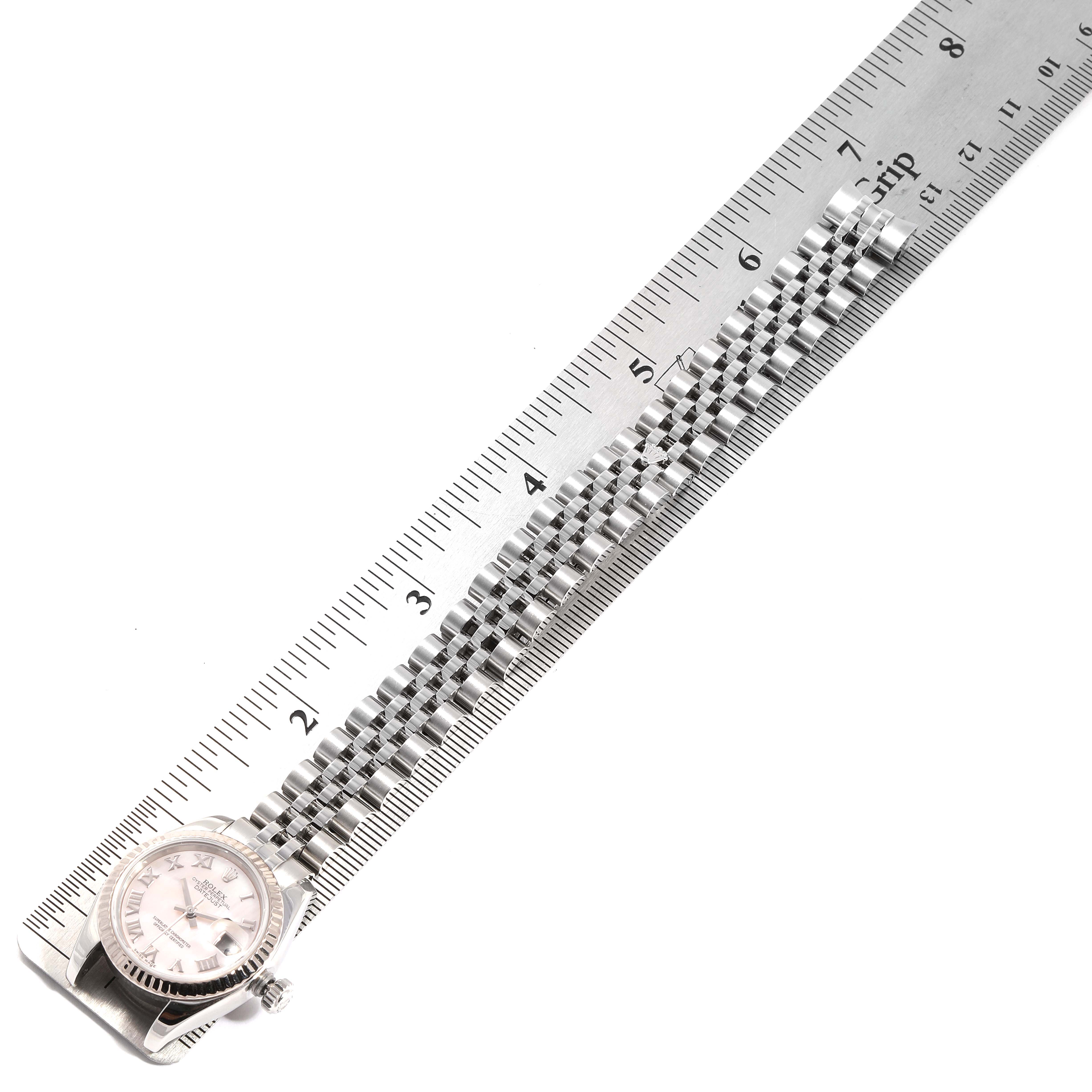 The image shows the face and bracelet of a Rolex Datejust 179174 Women
s Stainless Steel Mother of Pearl Dial 179174 Women
s Stainless Steel Mother of Pearl Dial watch, lying alongside a metal ruler angled from one end.