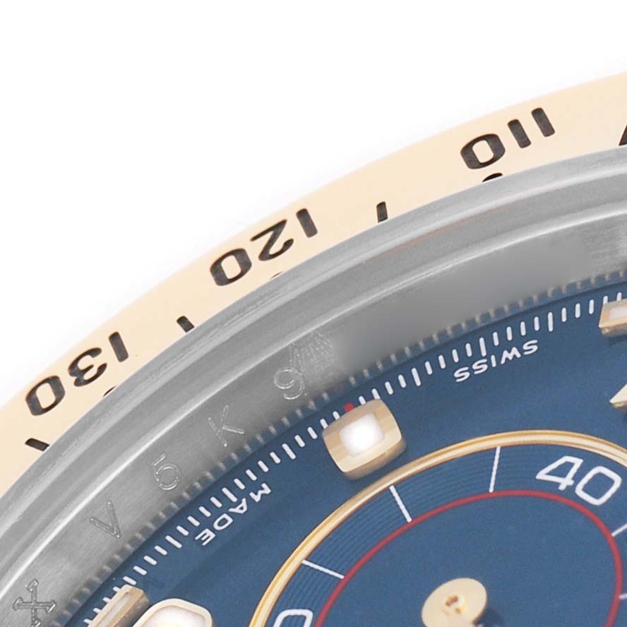 The image shows a close-up of the Rolex Daytona 116523 Men's Steel and Gold (two tone) Blue Dial's bezel and part of the dial, featuring tachymetric scale numbers.