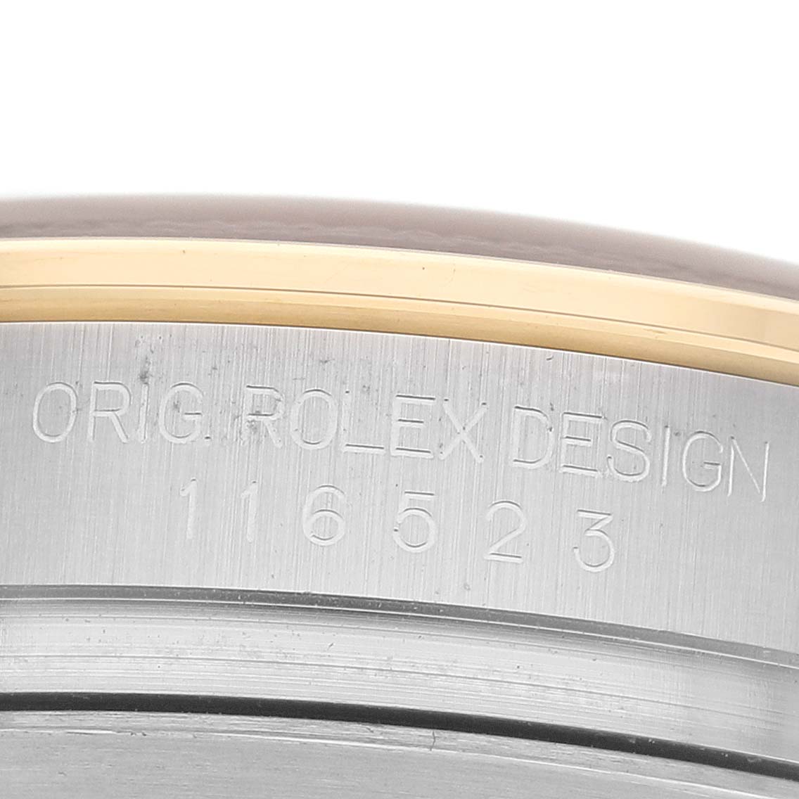 The image shows the side engraving on the case of a Rolex Daytona 116523 Men's Steel and Gold (two tone) Blue Dial, highlighting the inscription "ORIG ROLEX DESIGN" and model number.