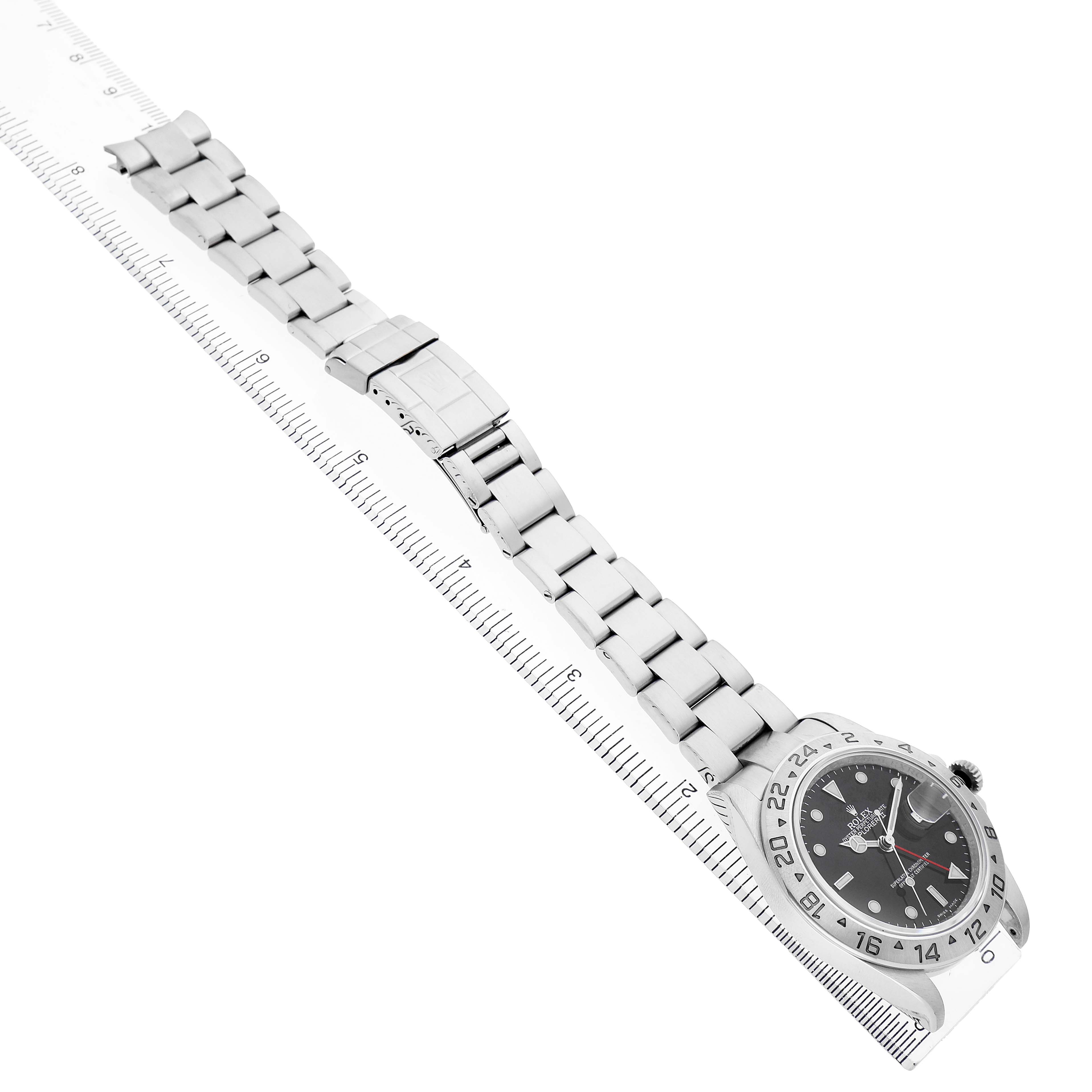 The Rolex Explorer 16570 Men's Stainless Steel Black Dial watch is shown diagonally, displaying its face, bezel, and full metal bracelet beside a ruler.