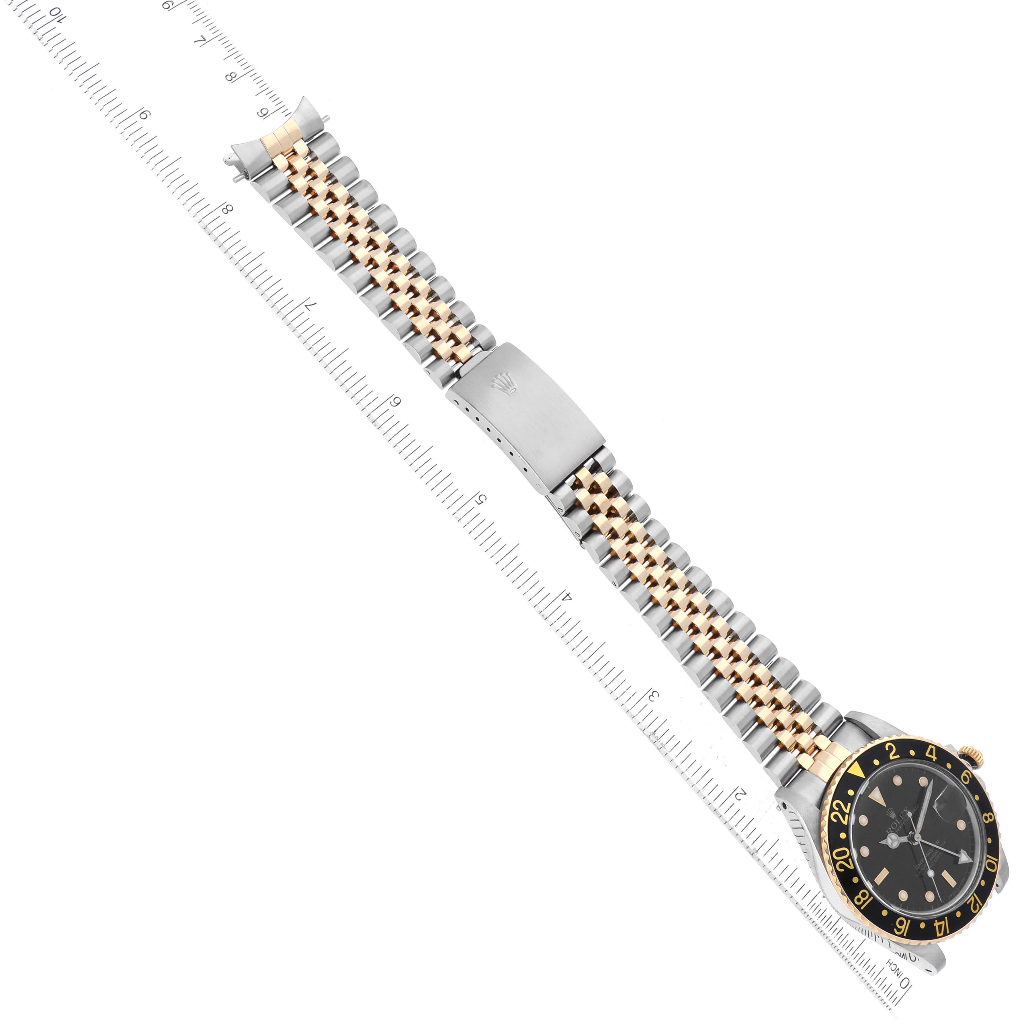 The image shows the entirety of a Rolex Vintage Collection 16753 Men's Steel and Gold (two tone) Black Dial 16753 Men's Steel and Gold (two tone) Black Dial model watch and its band, positioned diagonally with a ruler beside it.