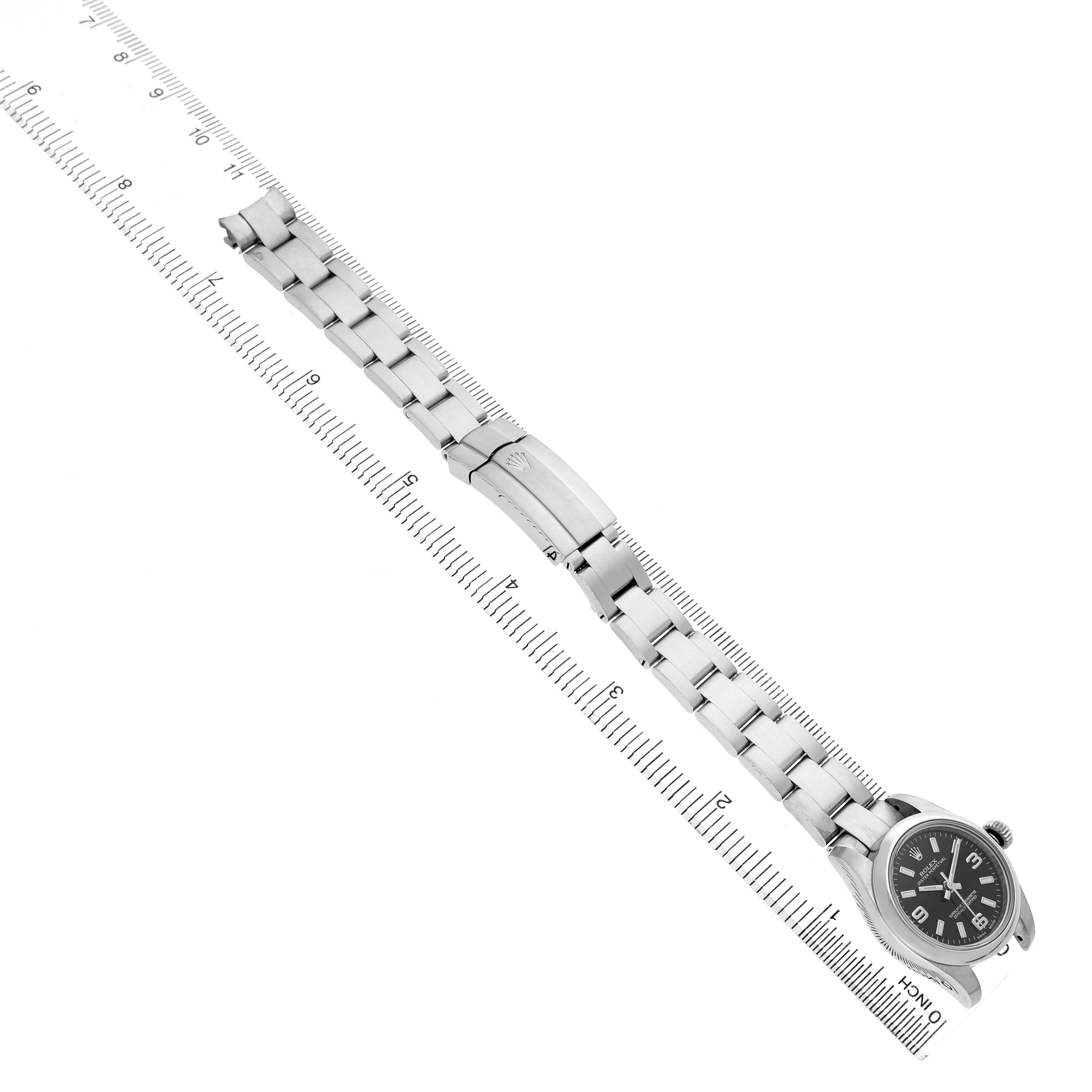 The Rolex Oyster Perpetual 176200 Women's Stainless Steel Black Dial watch is shown at a slight angle displaying the dial, bracelet, and clasp alongside a measuring ruler.