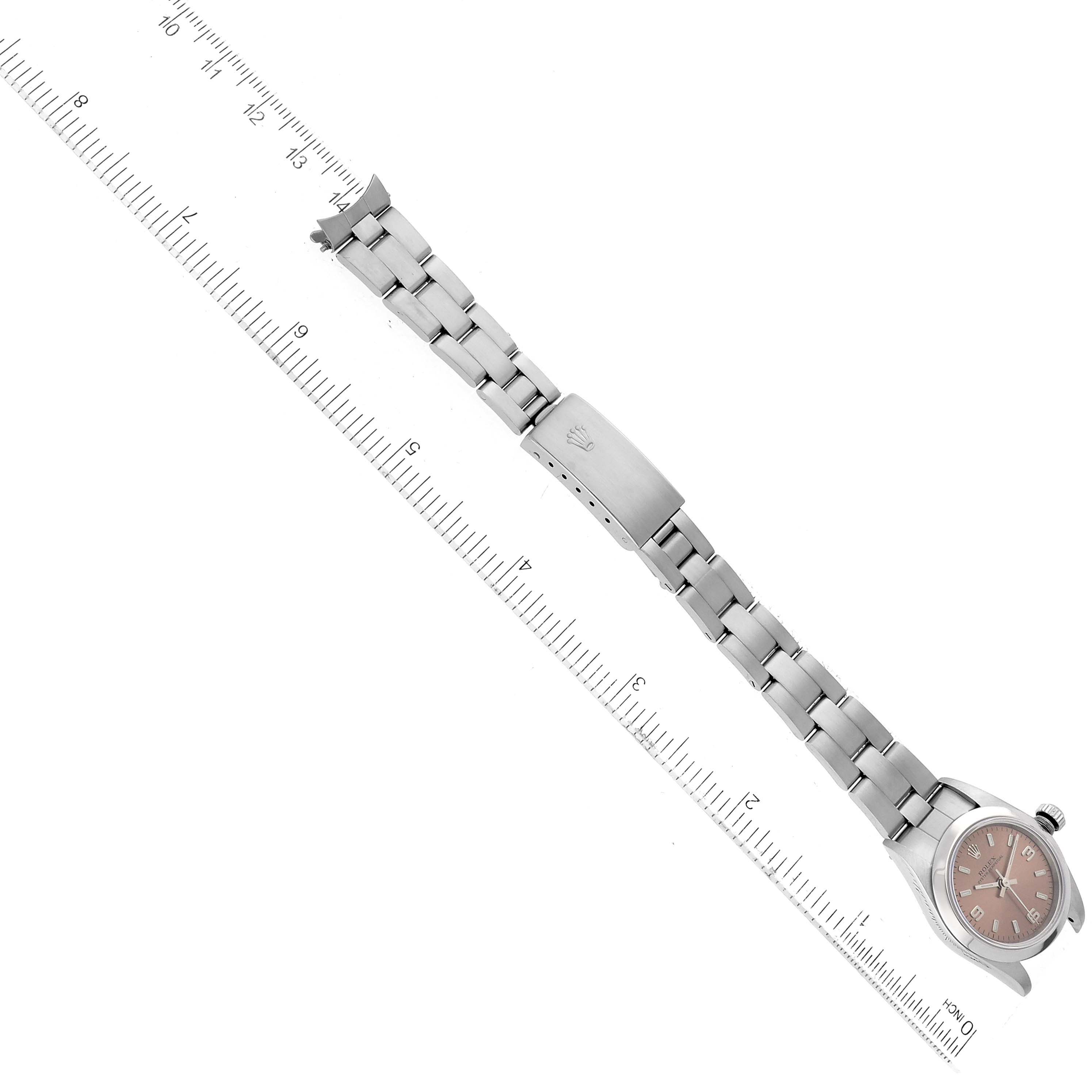 This image shows the full length of a Rolex Oyster Perpetual 76080 Women's Stainless Steel Pink Dial 76080 Women's Stainless Steel Pink Dial watch, positioned diagonally next to a measuring ruler.