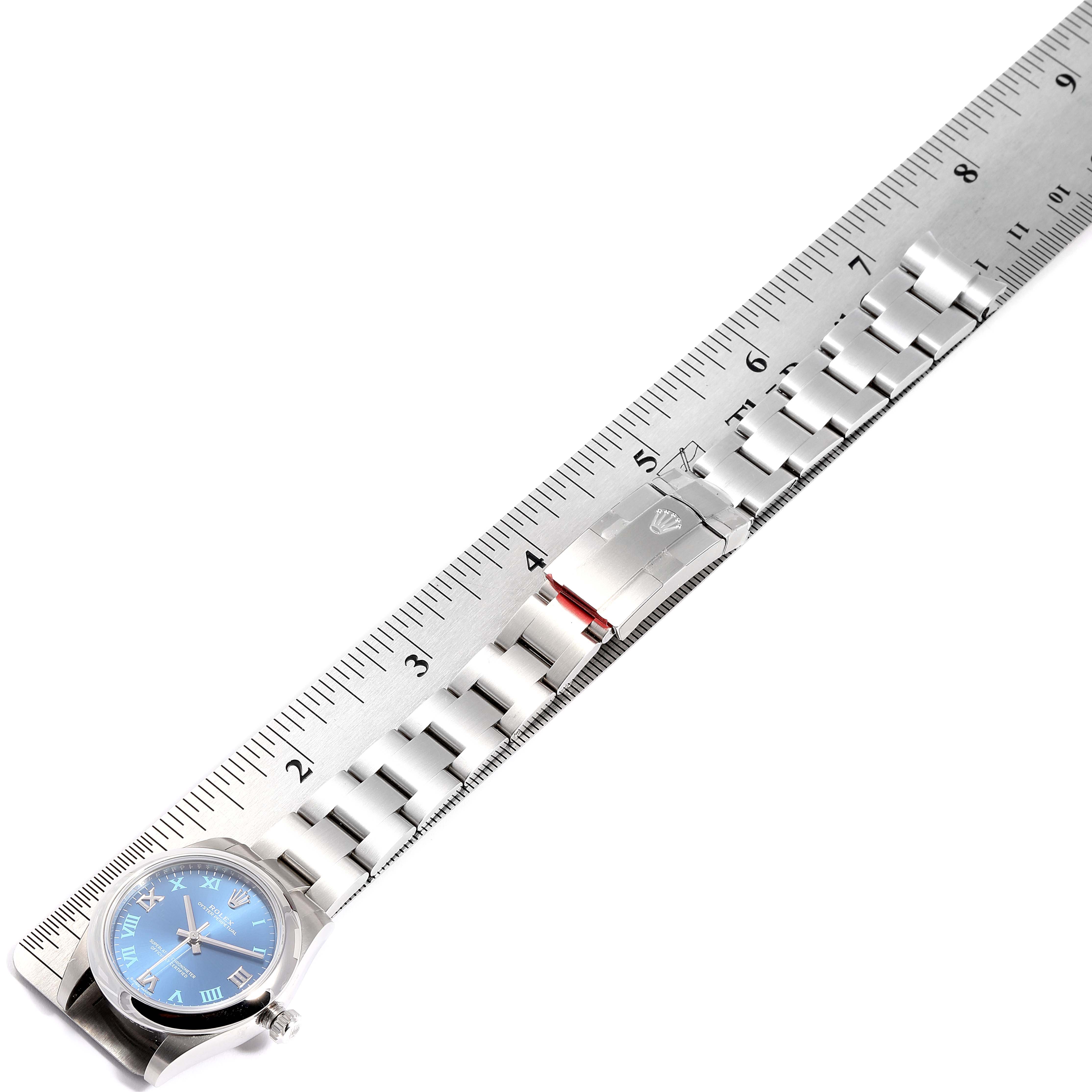 The image shows the Rolex Mid-Size 177200 Women
s Stainless Steel Blue Dial 177200 Women
s Stainless Steel Blue Dial model watch lying flat against a ruler, displaying the face, bracelet, and clasp.