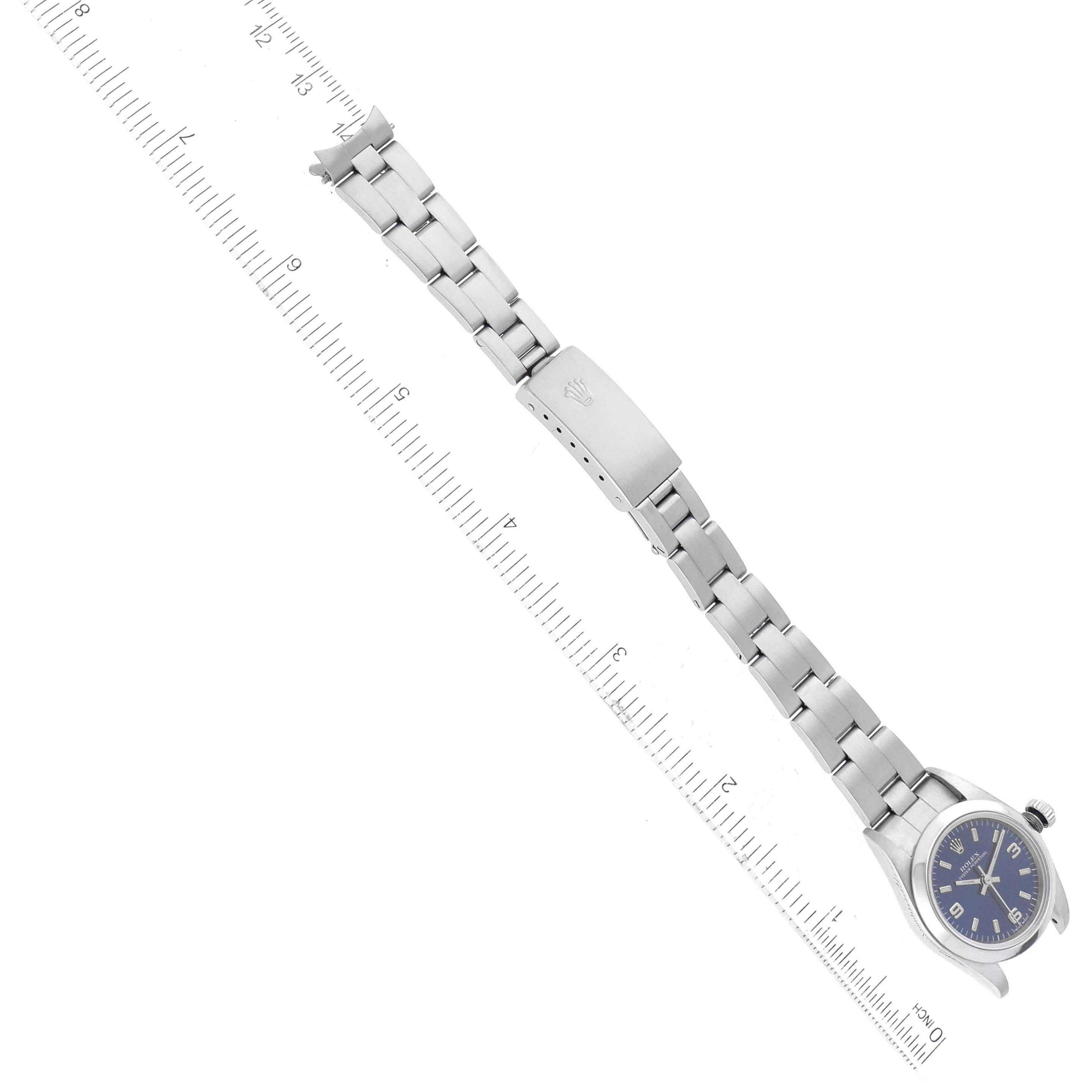 The image shows a top-down view of a Rolex Oyster Perpetual 76080 Women's Stainless Steel Blue Dial 76080 Women's Stainless Steel Blue Dial watch, highlighting the watch face, bracelet, and clasp alongside a ruler.