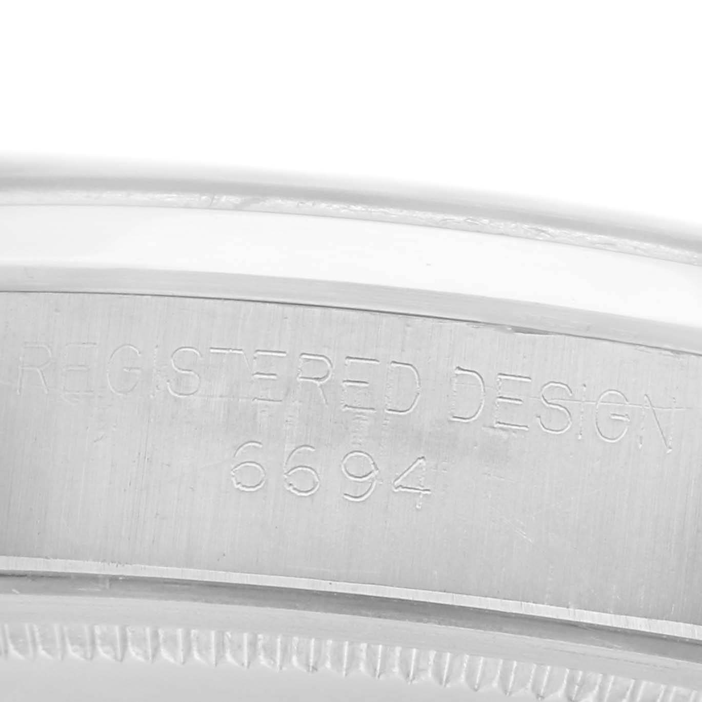 The image shows an engraved close-up of the casing of a Rolex Date watch, model number 6694, with the inscription "REGISTERED DESIGN."
