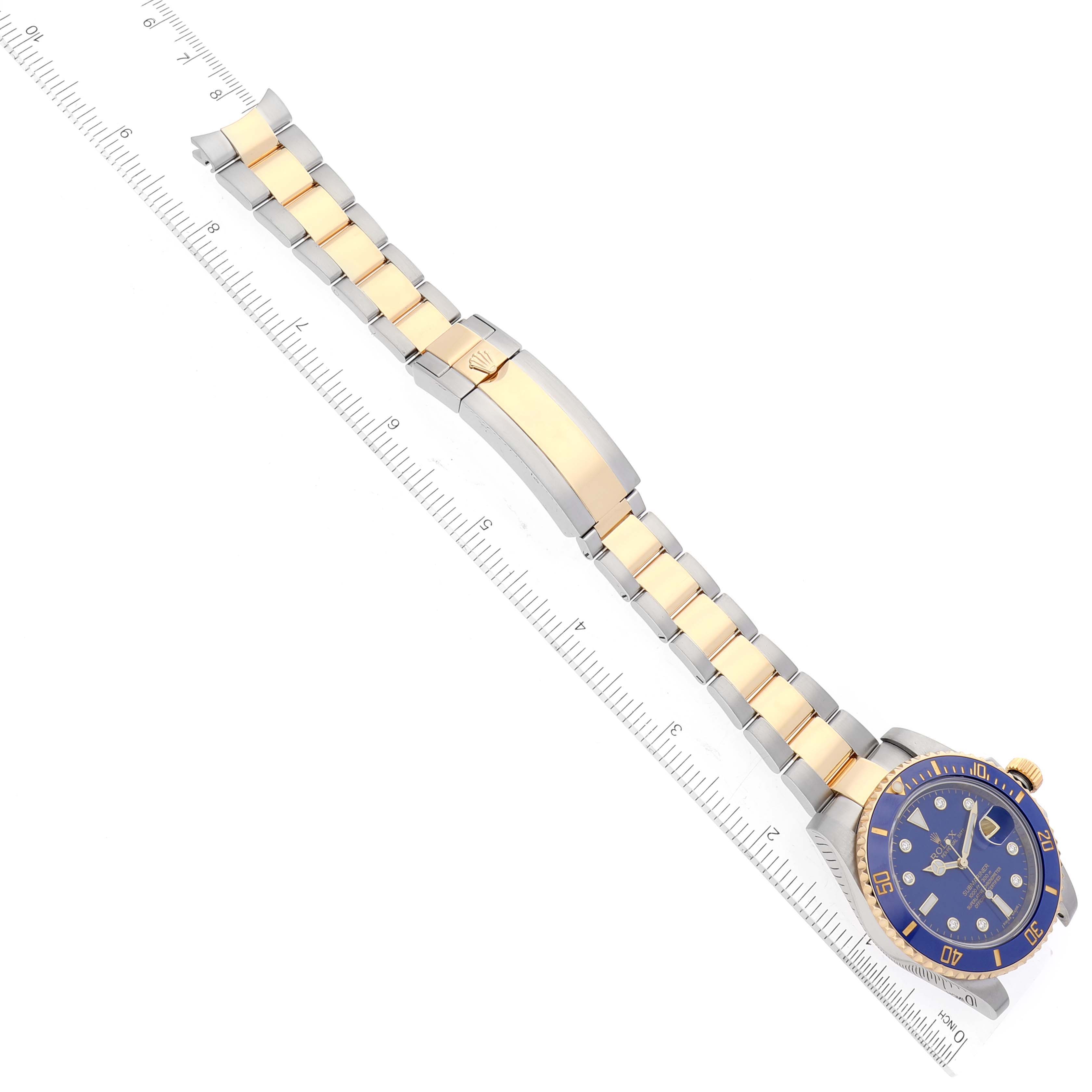 The image shows a Rolex Submariner 116613 Men
s Steel and Gold (two tone) Blue Dial 116613 Men
s Steel and Gold (two tone) Blue Dial watch at an angle with its blue and gold bezel, dial, and two-tone bracelet aligned next to a ruler.