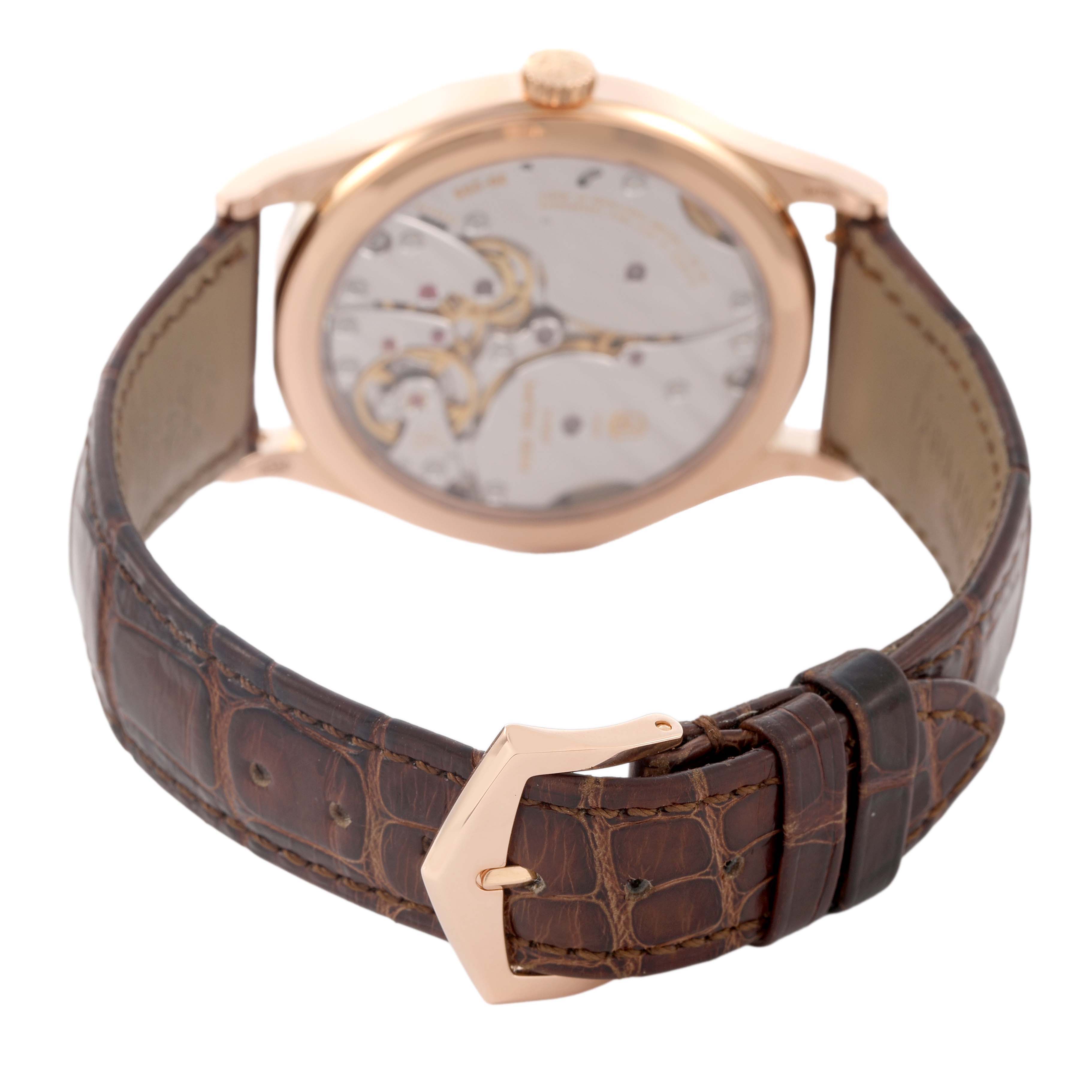 The image shows the back view of a Patek Philippe Calatrava 6119R-001 Men's Rose Gold Silver Dial, highlighting the movement and a brown leather strap with a buckle.
