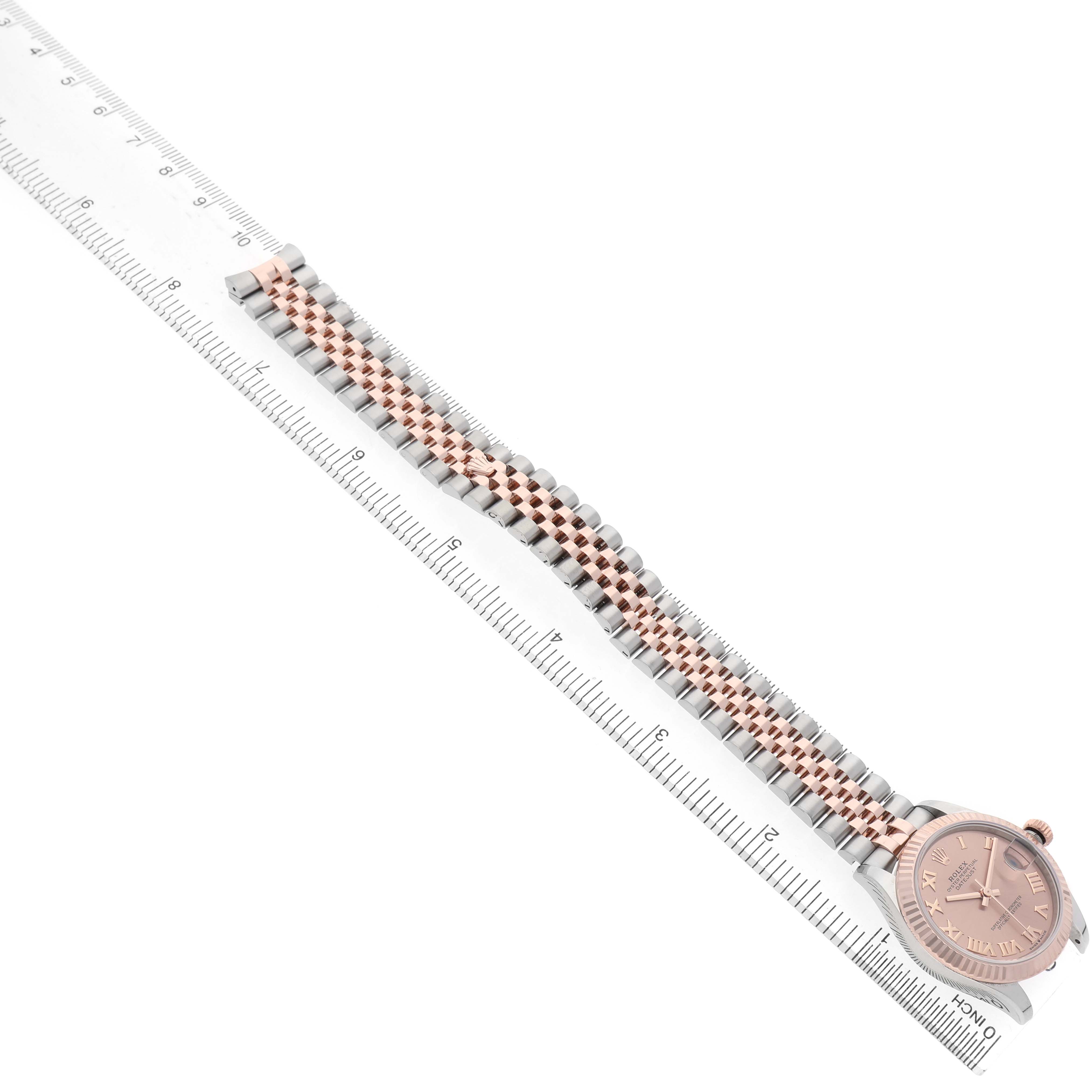 The Rolex Mid-Size 278271 Women's Steel and Gold (two tone) Pink Dial watch is shown at an angle, featuring its bracelet and bezel alongside a ruler for scale.