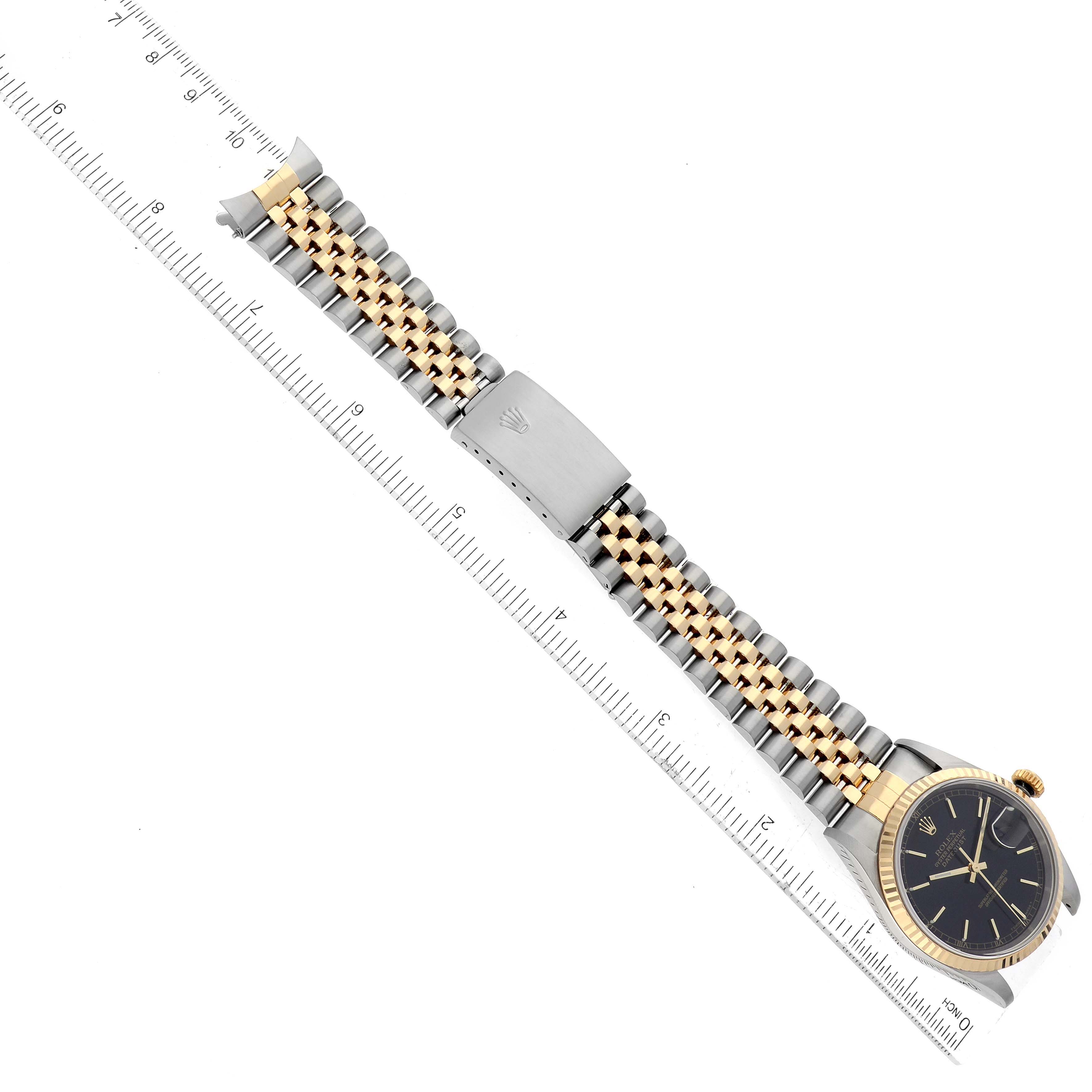 The image shows a Rolex Datejust 16233 Men's Steel and Gold (two tone) Black Dial 16233 Men's Steel and Gold (two tone) Black Dial watch displayed horizontally, highlighting its bracelet and clasp, with a ruler for scale.