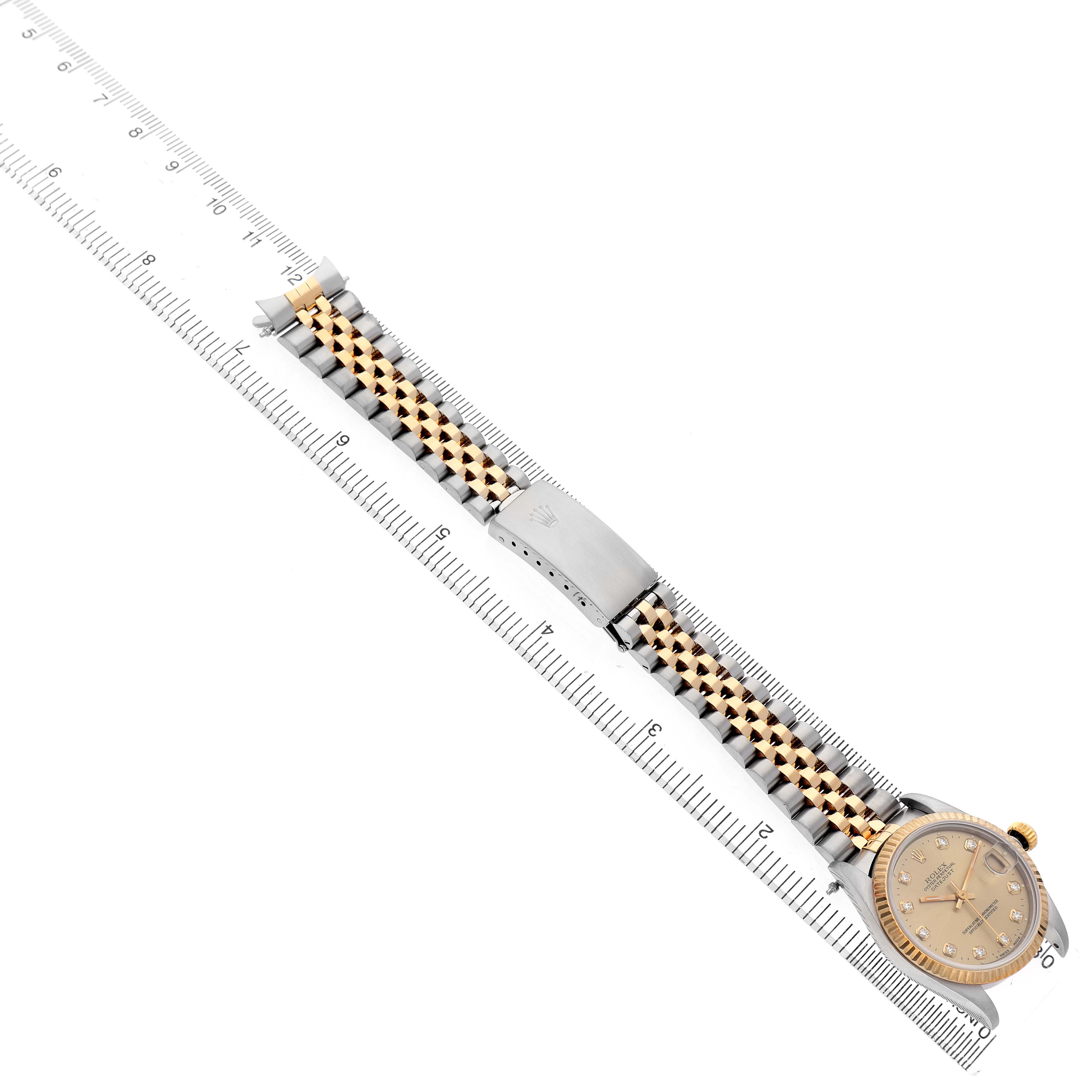 The Rolex Mid-Size 68273 Women's Steel and Gold (two tone) Champagne Dial watch is shown at an angle, displaying its band, clasp, and face placed alongside a ruler for scale.